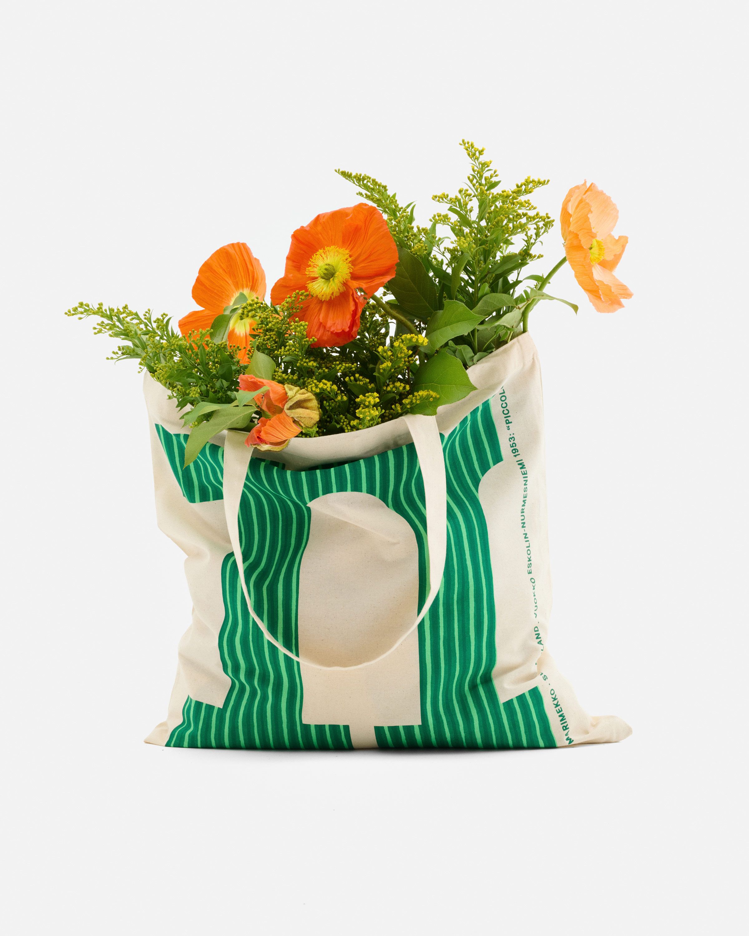 Logo tote, with a green letter M in Piccolo print, filled with flowers.