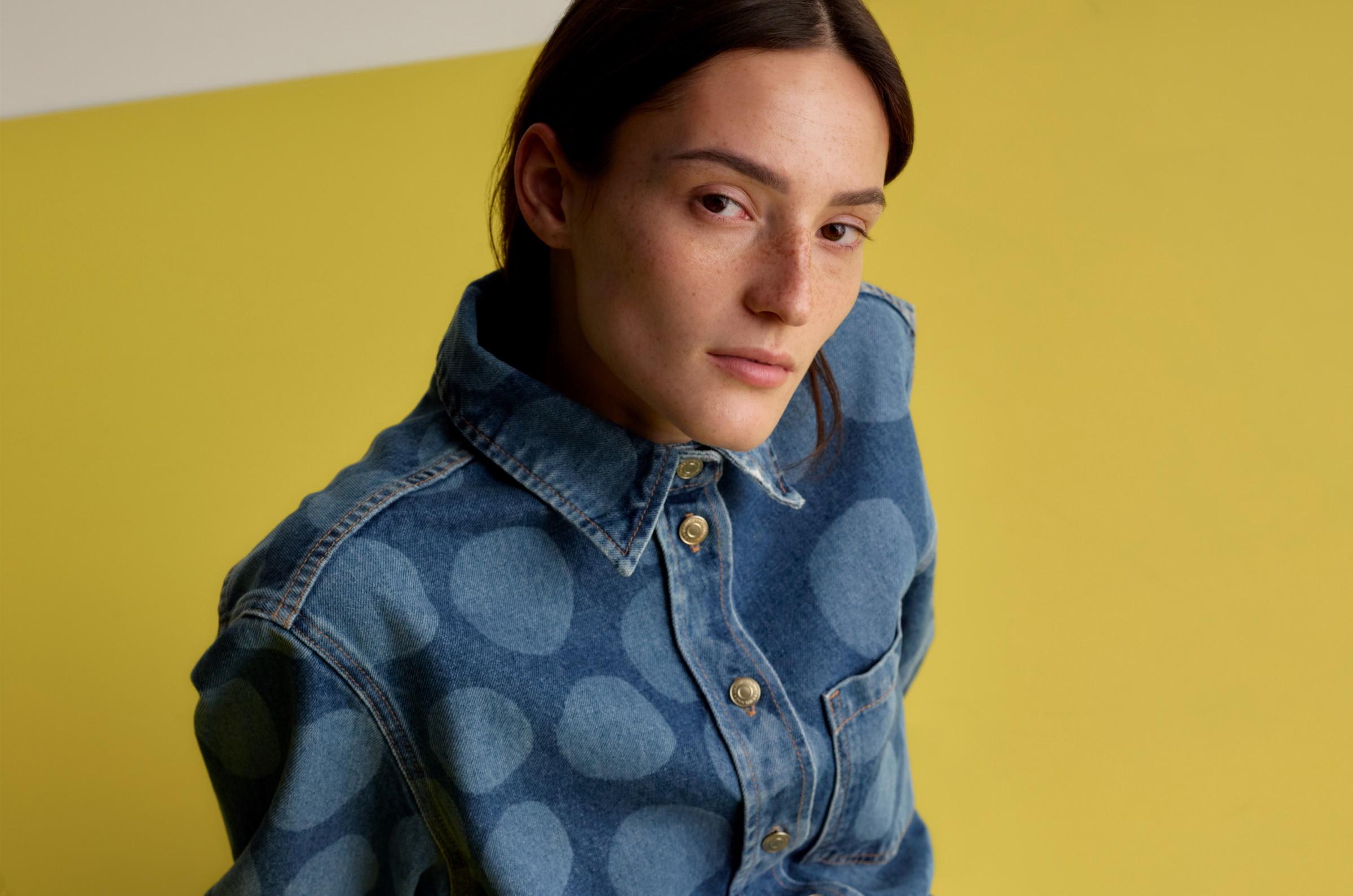 Model sitting on the floor, wearing a matching denim shirt and mini skirt in Petrooli print, and a brown leather belt with Unikko detail.