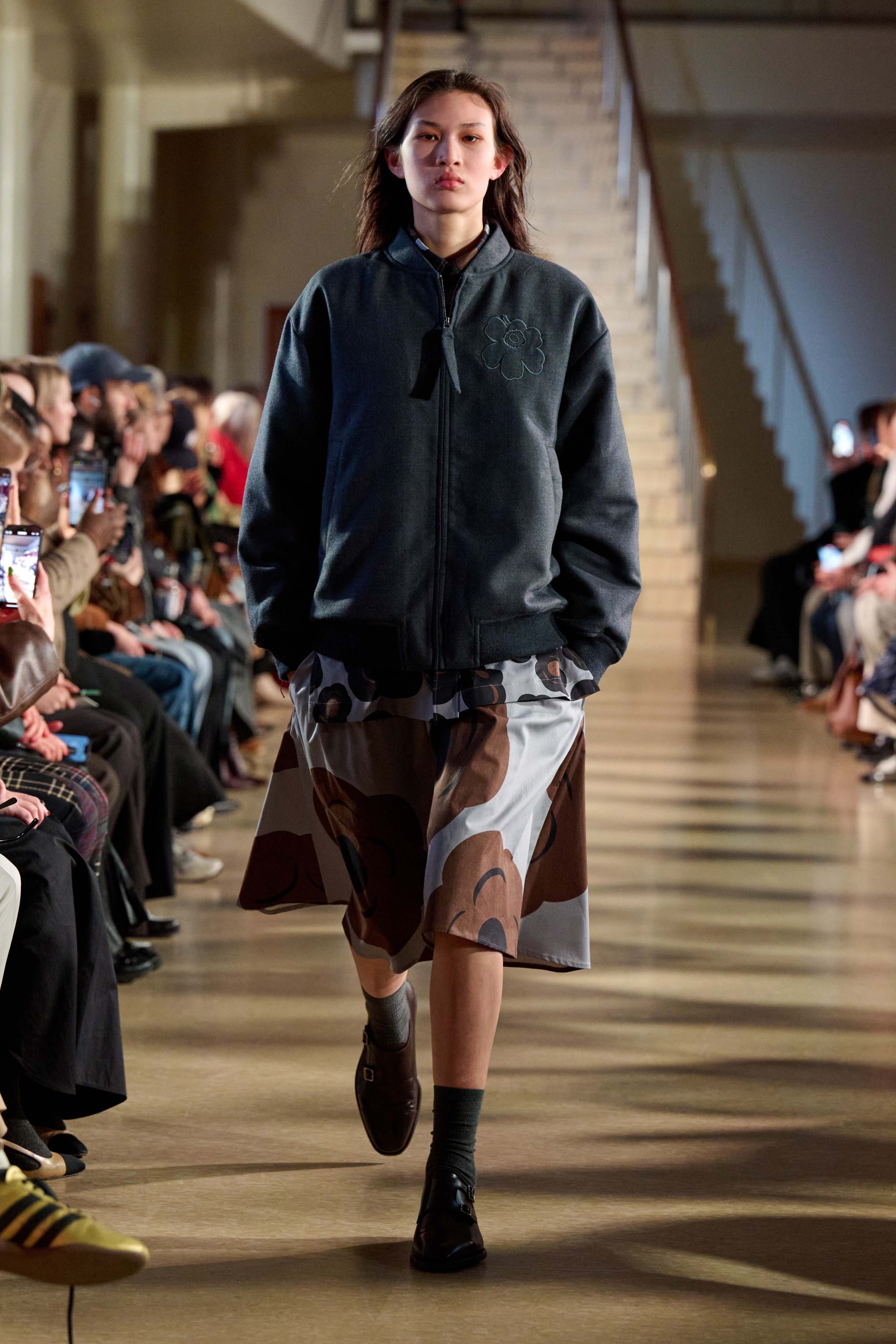 A model walks in the Marimekko fashion show wearing a gray Unikko-coat and Tumma-printed dress