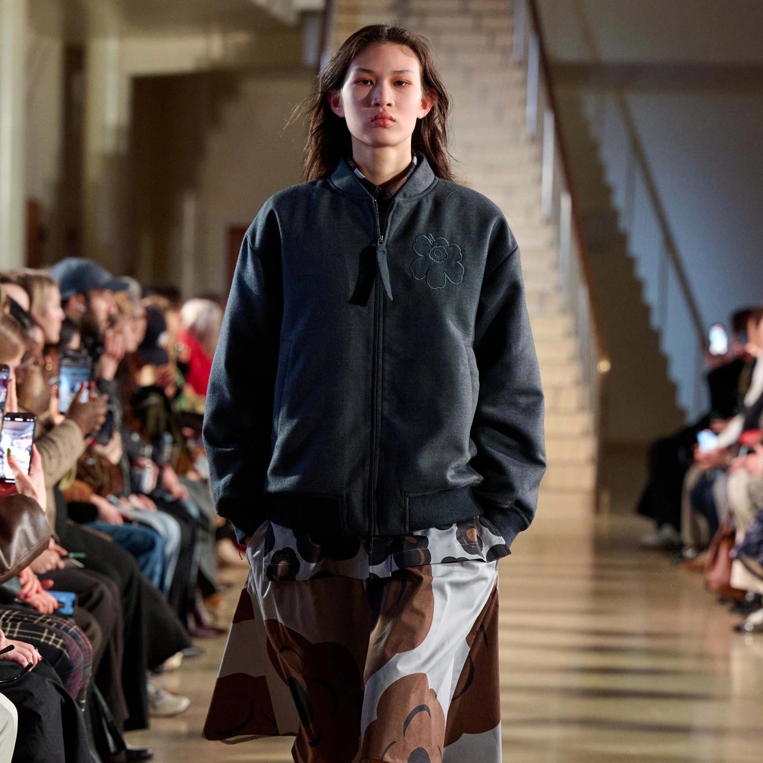 A model walks in the Marimekko fashion show wearing a gray Unikko-coat and Tumma-printed dress