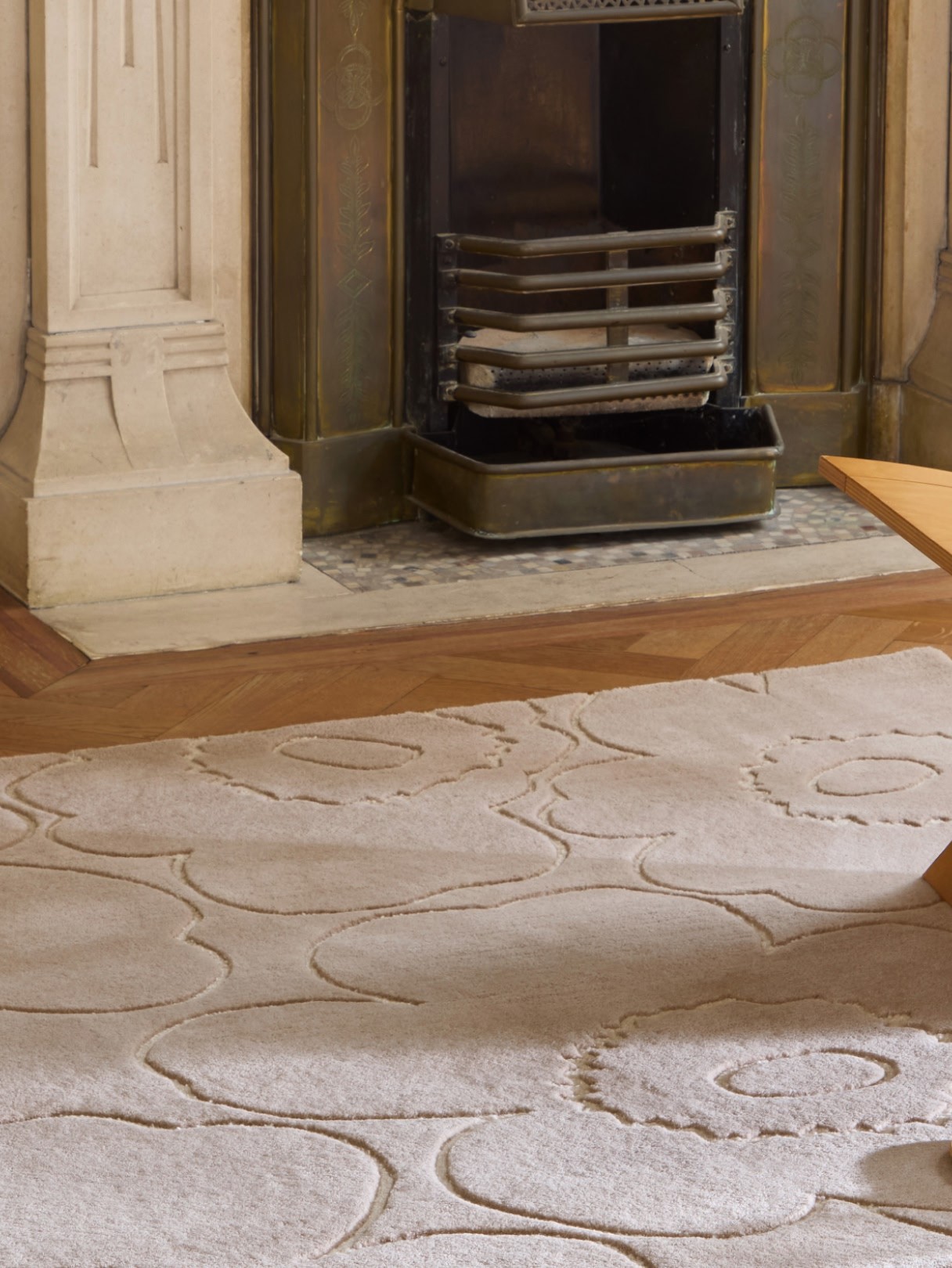 Beige rug with Piirto Unikko pattern in front of a fireplace and Urna vase on the side with flowers.