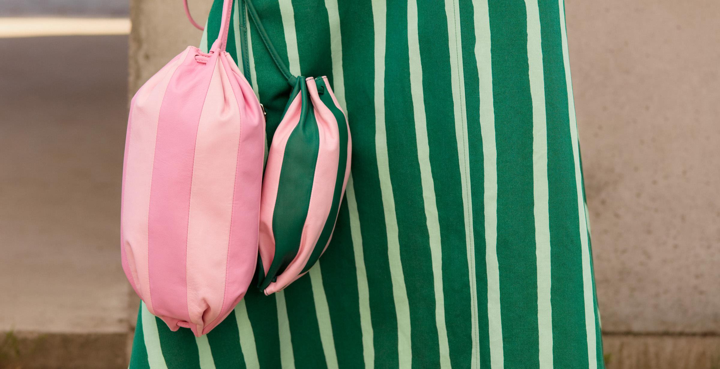 Model holding a pink Karla Multi and a green Pikku Karla Multi leather bag.