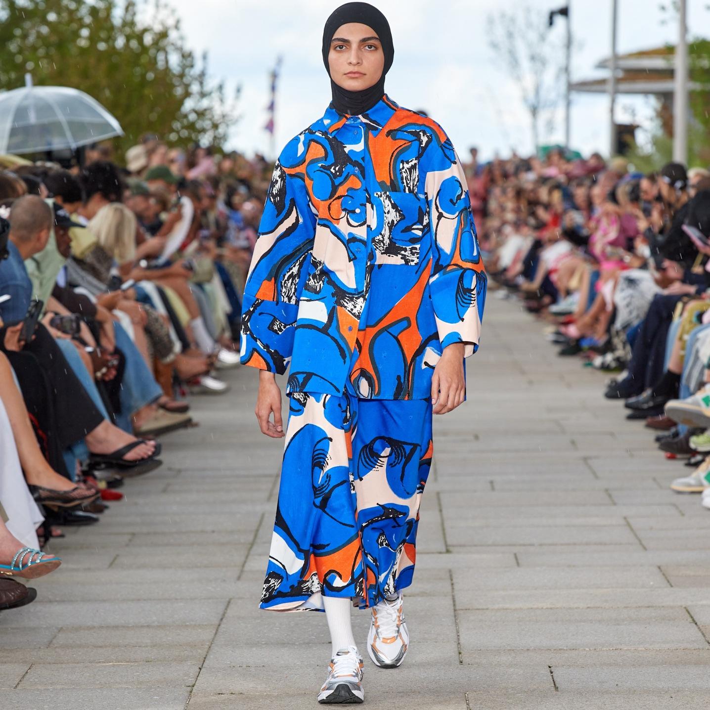 Model walking on the catwalk of the fashion show wearing a Kukkavera Eldfamn shirt and skirt.