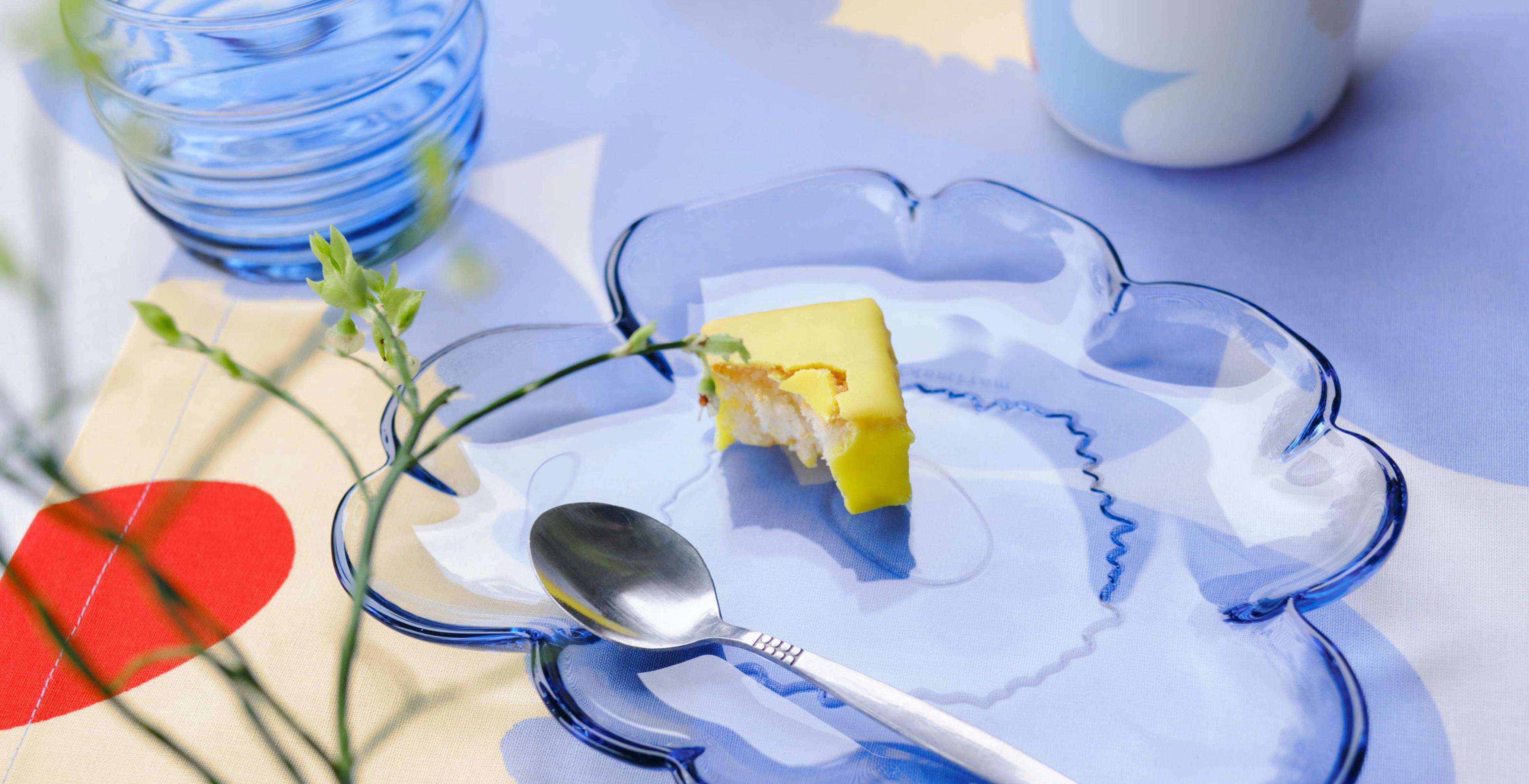 Outdoor table setting with blue Sukat Makkaralla glasses, blue Unikko-shaped glass plate and mini vases on a Unikko print tablecloth.