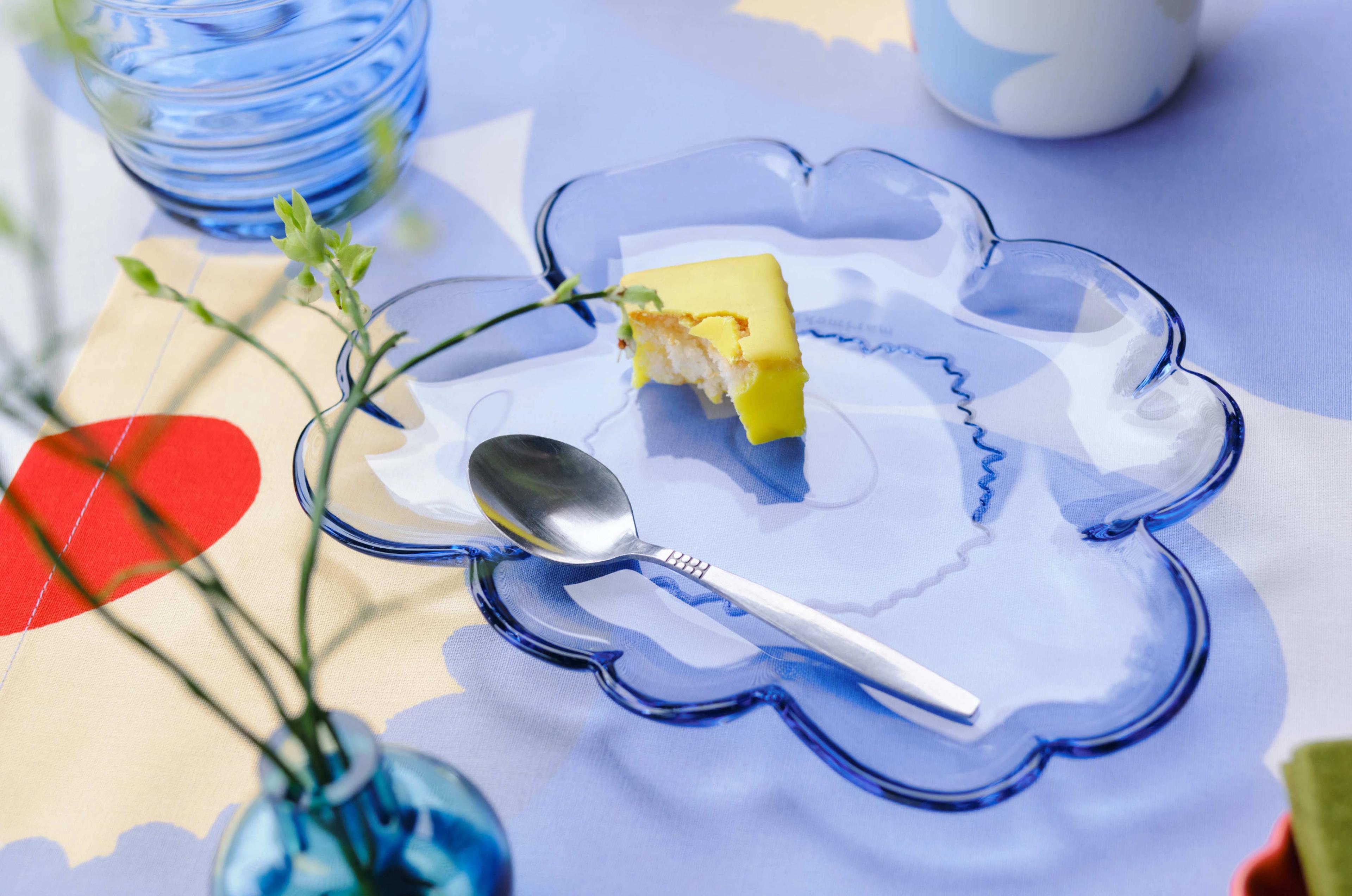 Kattaus, jossa on sininen Unikko-muotoinen lasilautanen, muki Unikko-painatuksella ja sininen Mini lasimaljakko.