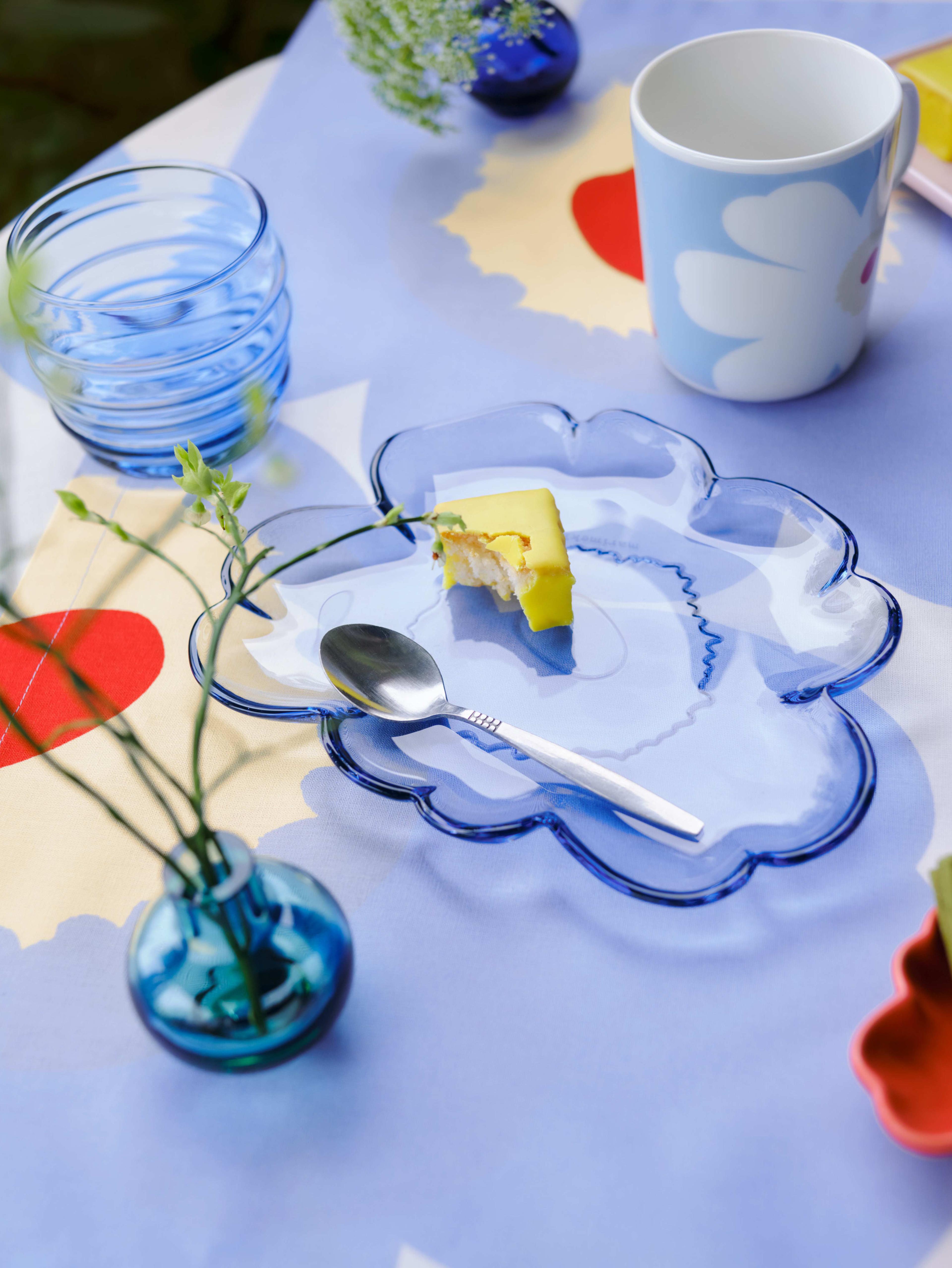 Outdoor table setting with blue Sukat Makkaralla glasses, blue Unikko-shaped glass plate and mini vases on a Unikko print tablecloth.