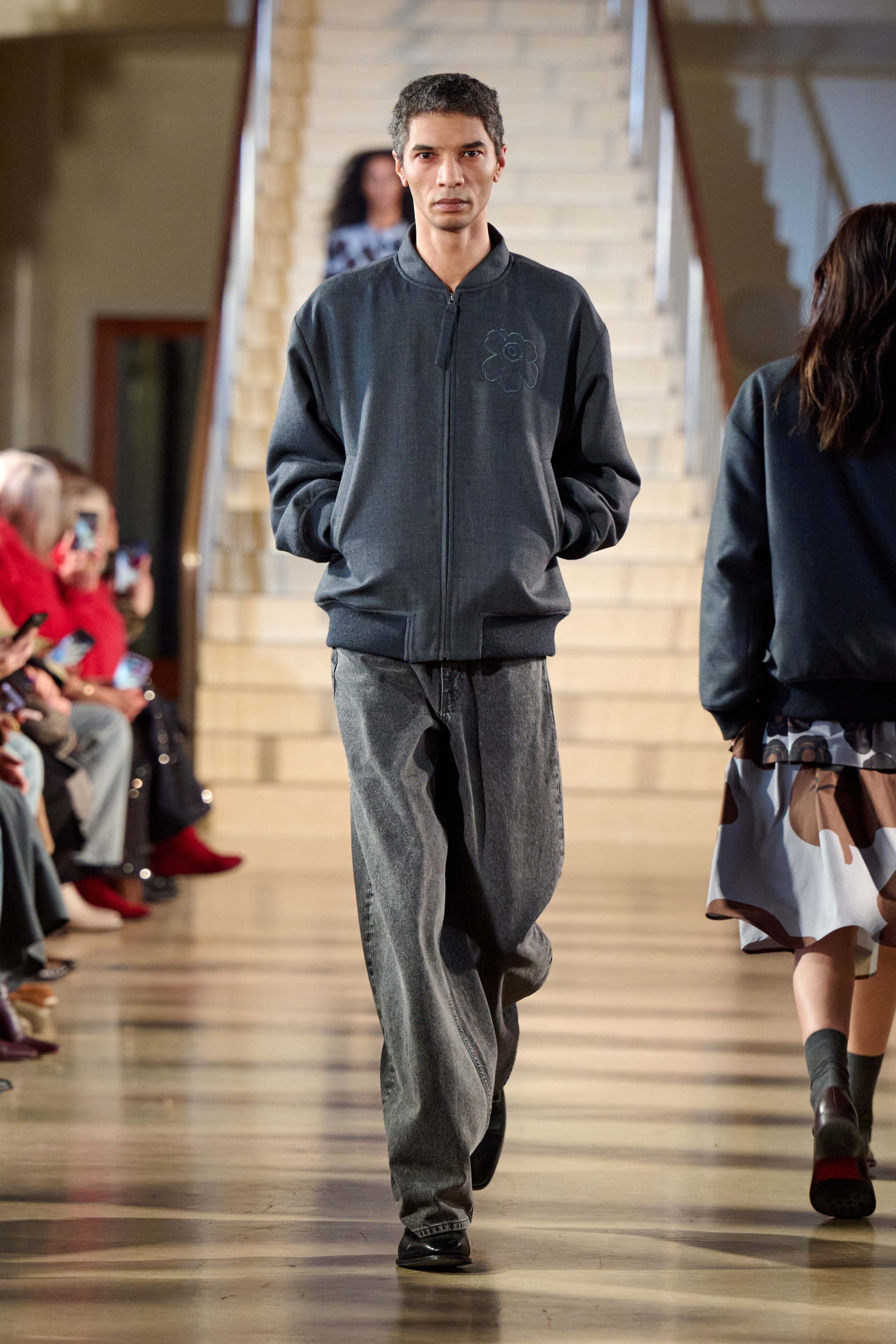 A male model walks in the Marimekko fashion show wearing a gray Unikko coat and Maridenim jeans