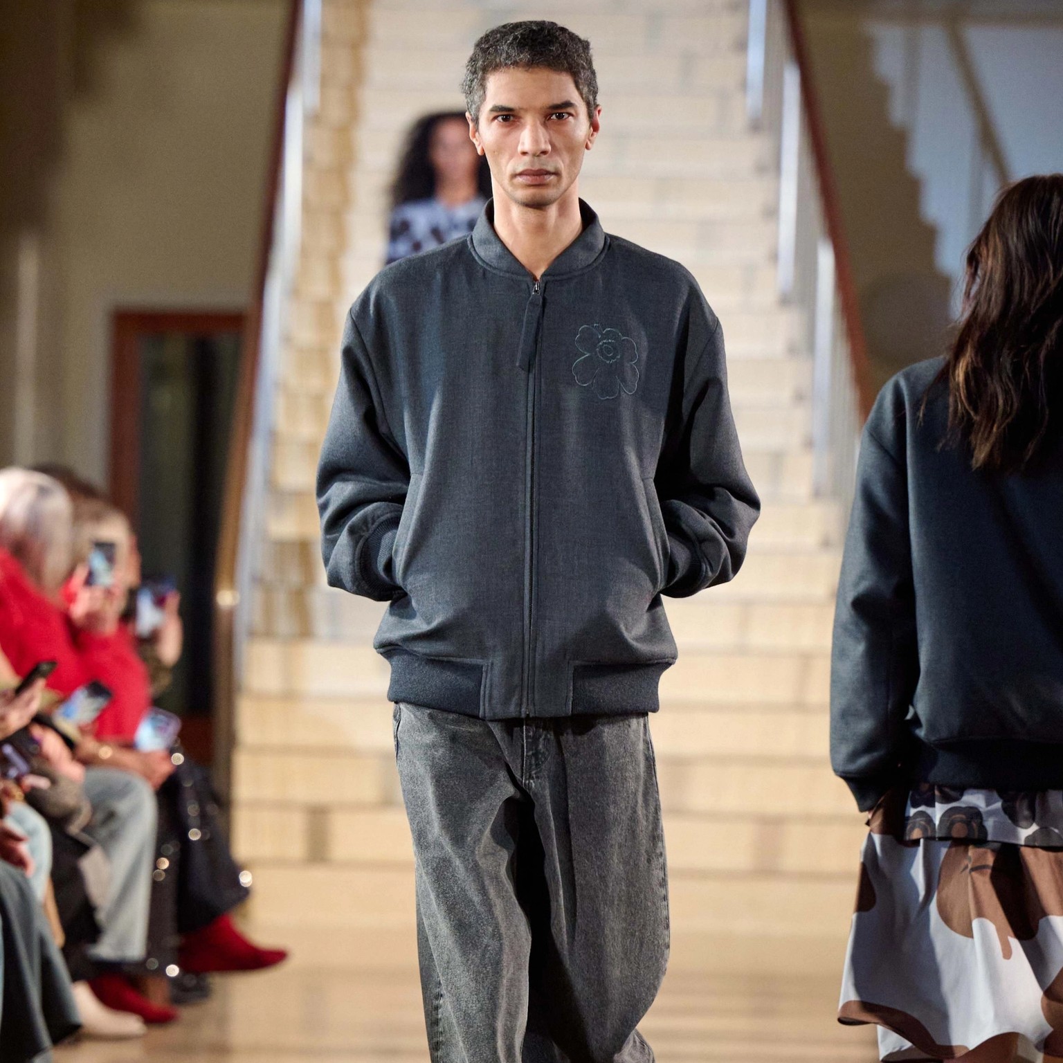 A male model walks in the Marimekko fashion show wearing a gray Unikko coat and Maridenim jeans