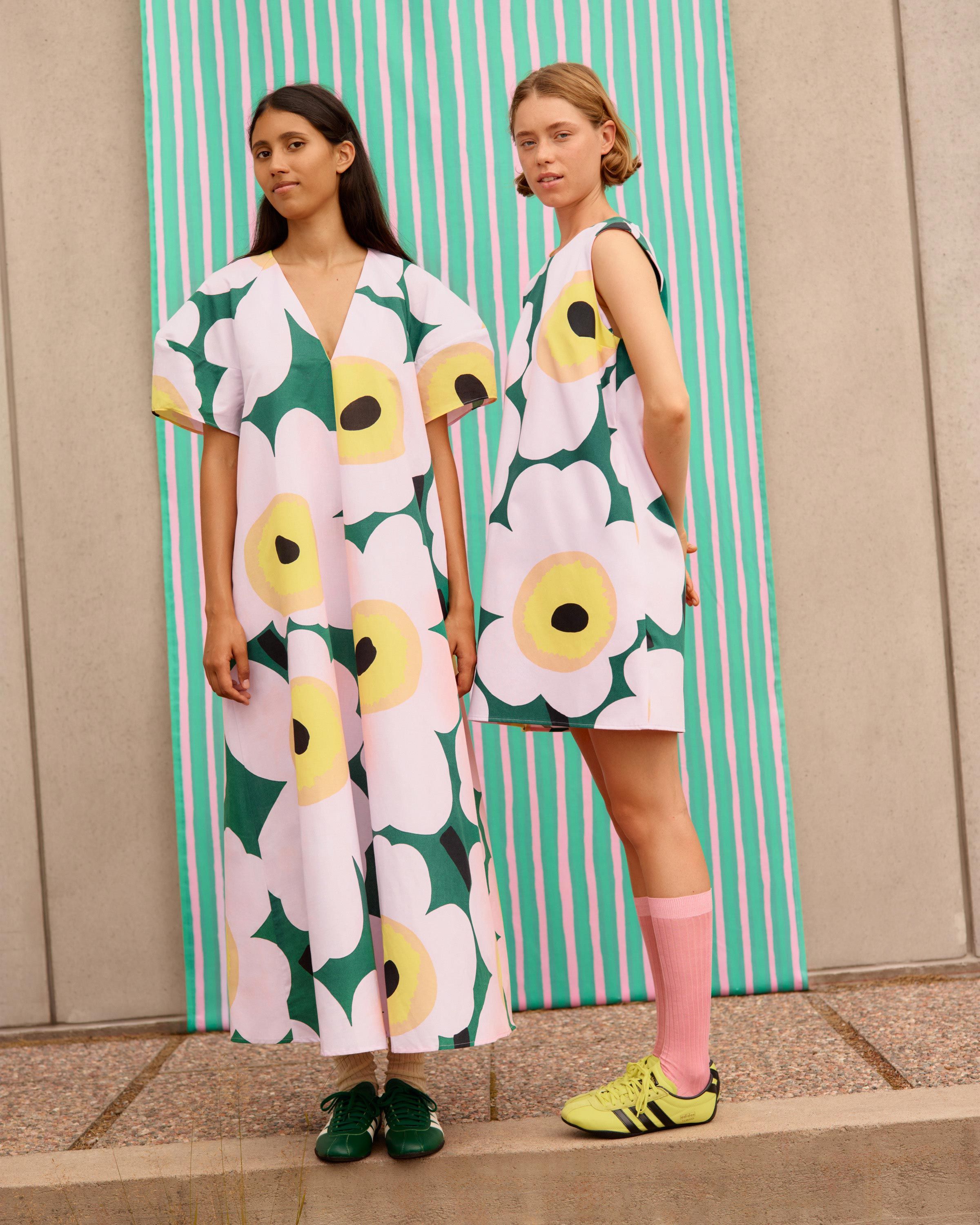 Models wearing green and pink Unikko dresses in front of light green Piccolo fabric.