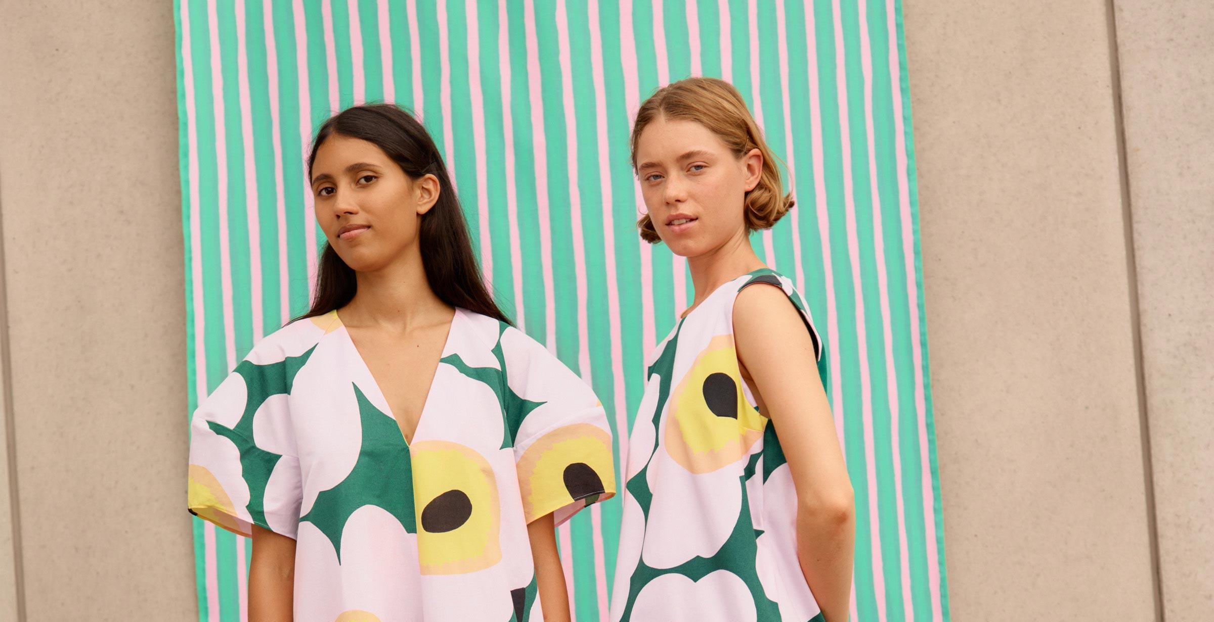 Models wearing green and pink Unikko dresses in front of light green Piccolo fabric.