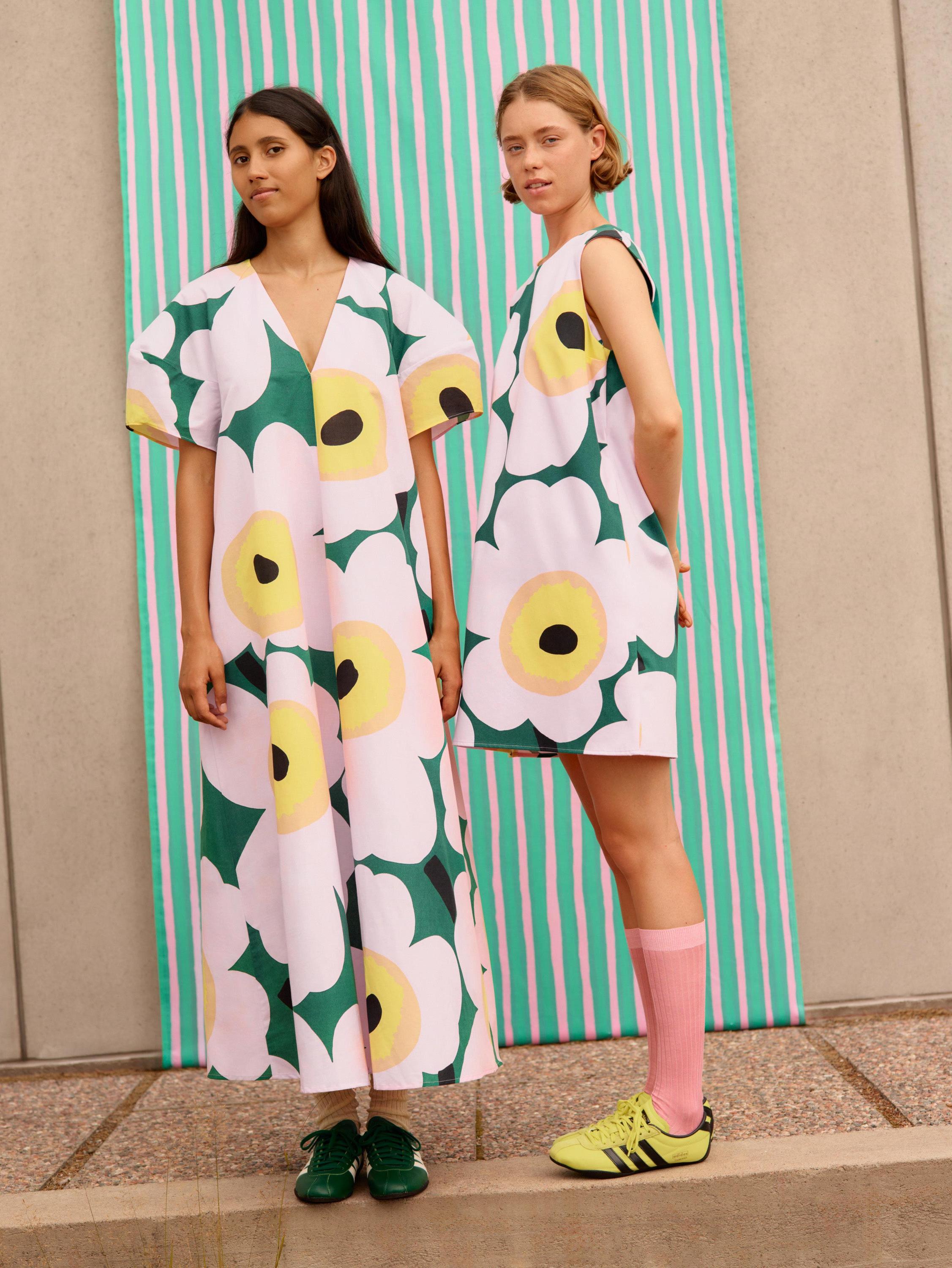 Models wearing green and pink Unikko dresses in front of light green Piccolo fabric.