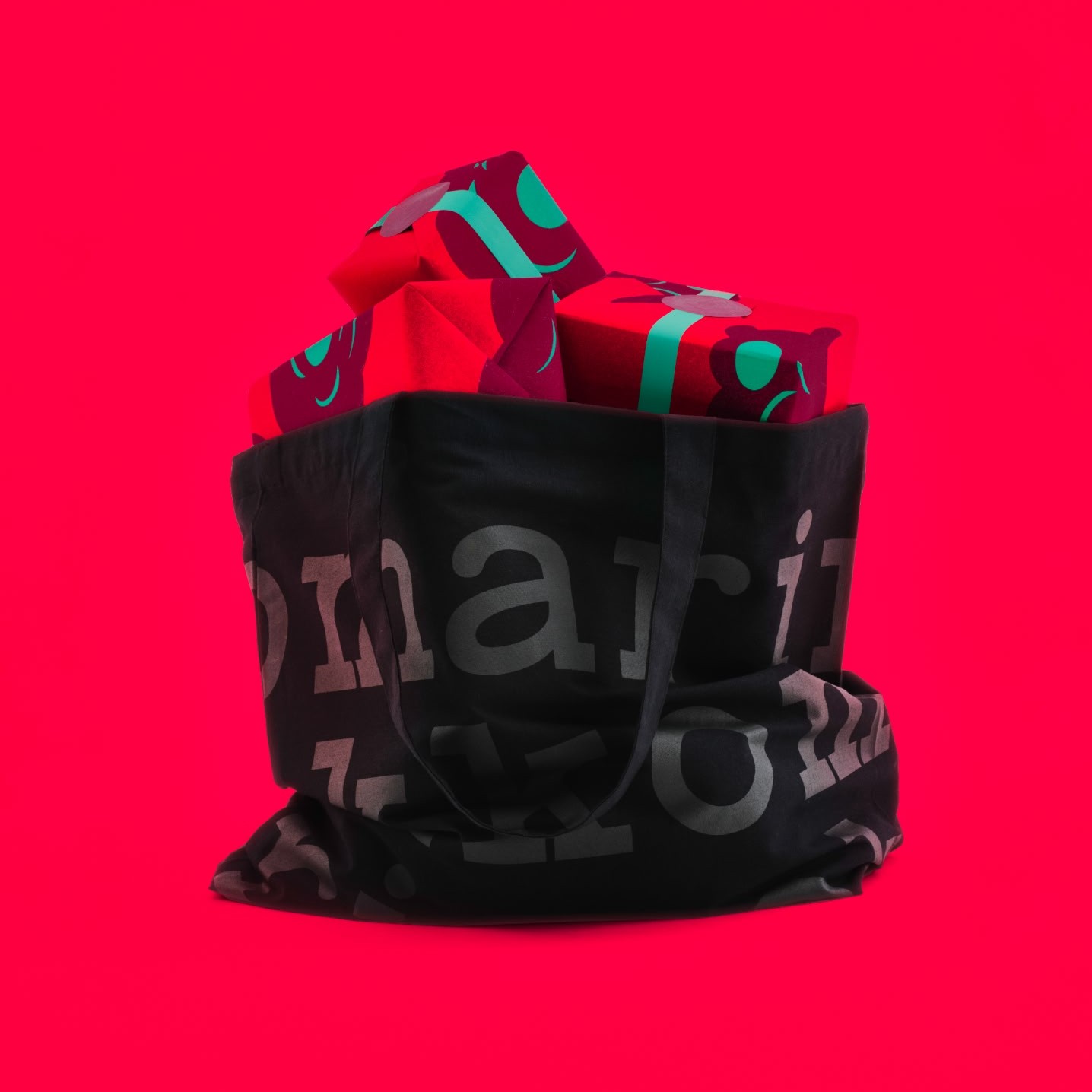 Musta Marimekko-logolla varustettu kangaskassi punaisella taustalla.