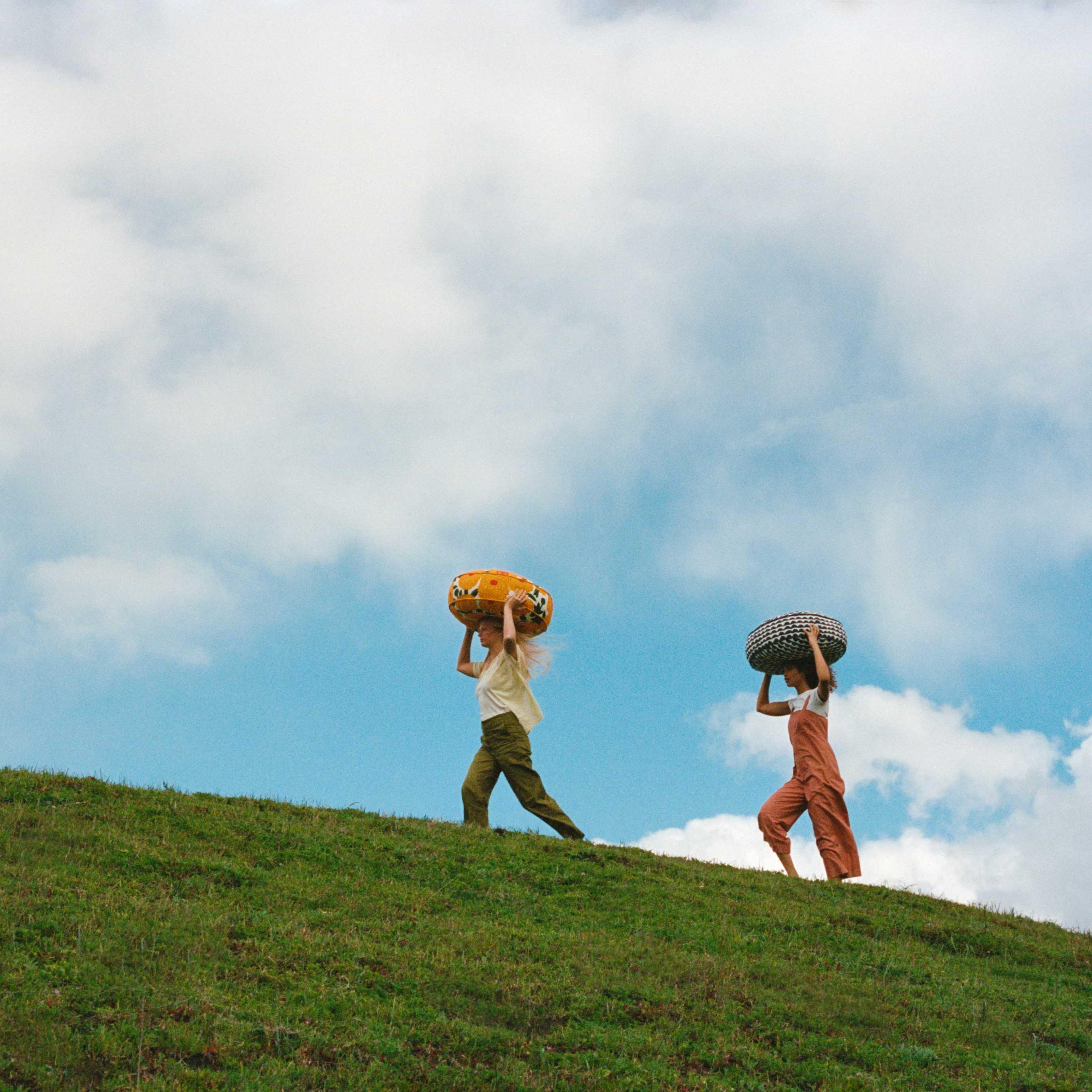 Modelle mit Kissen aus der Zusammenarbeit von West Elm und Marimekko auf einer grünen Wiese