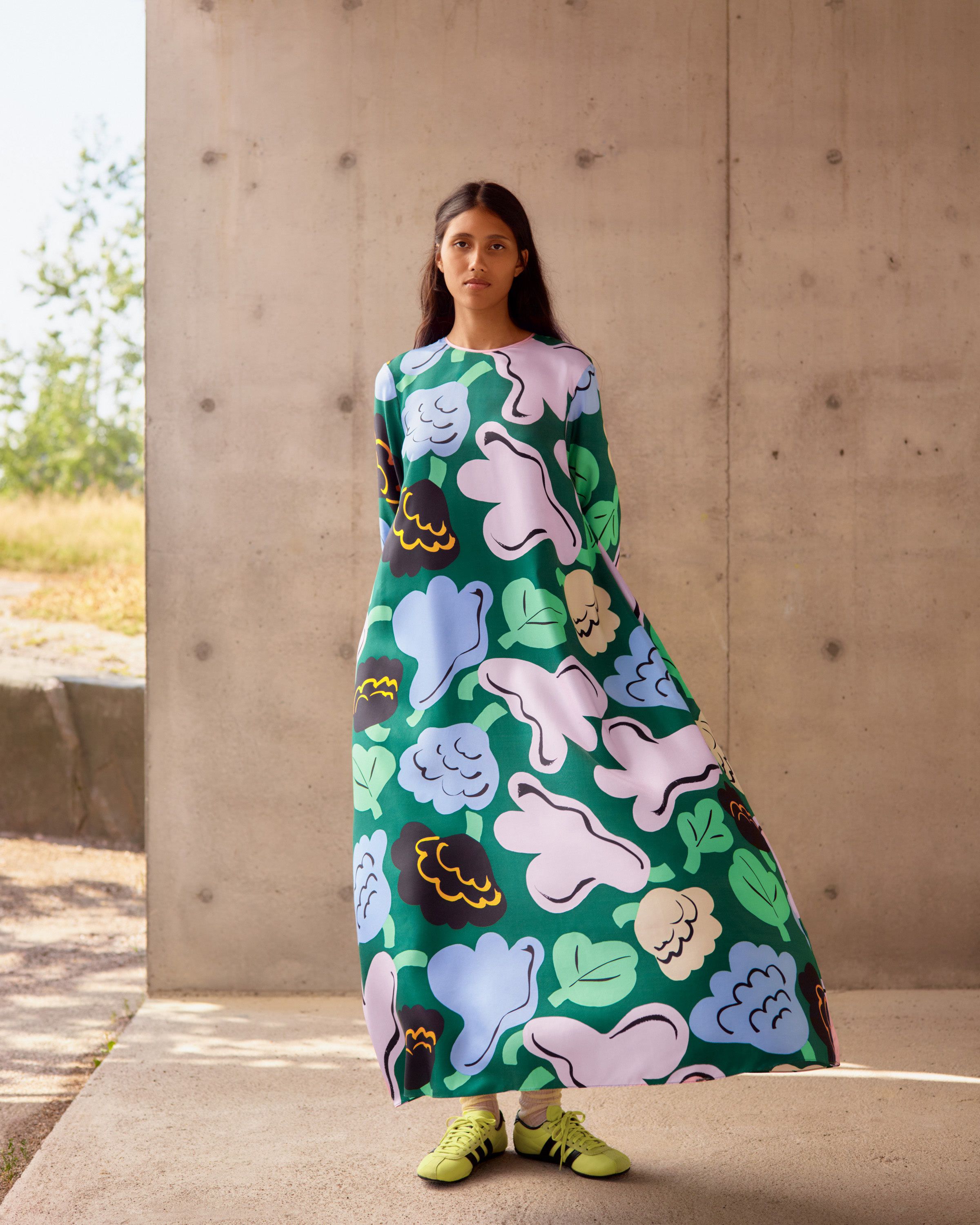 Model posing in front of a concrete wall with a green flower dress in Kukasta kukkaan print.
