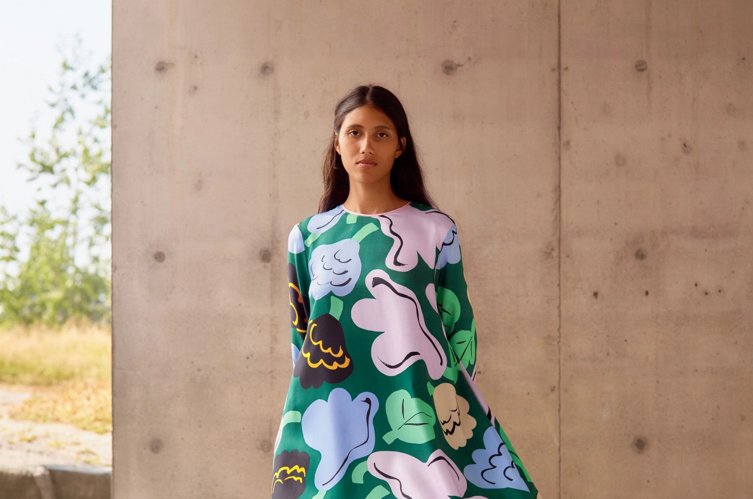 Model posing in front of a concrete wall with a green flower dress in Kukasta kukkaan print.