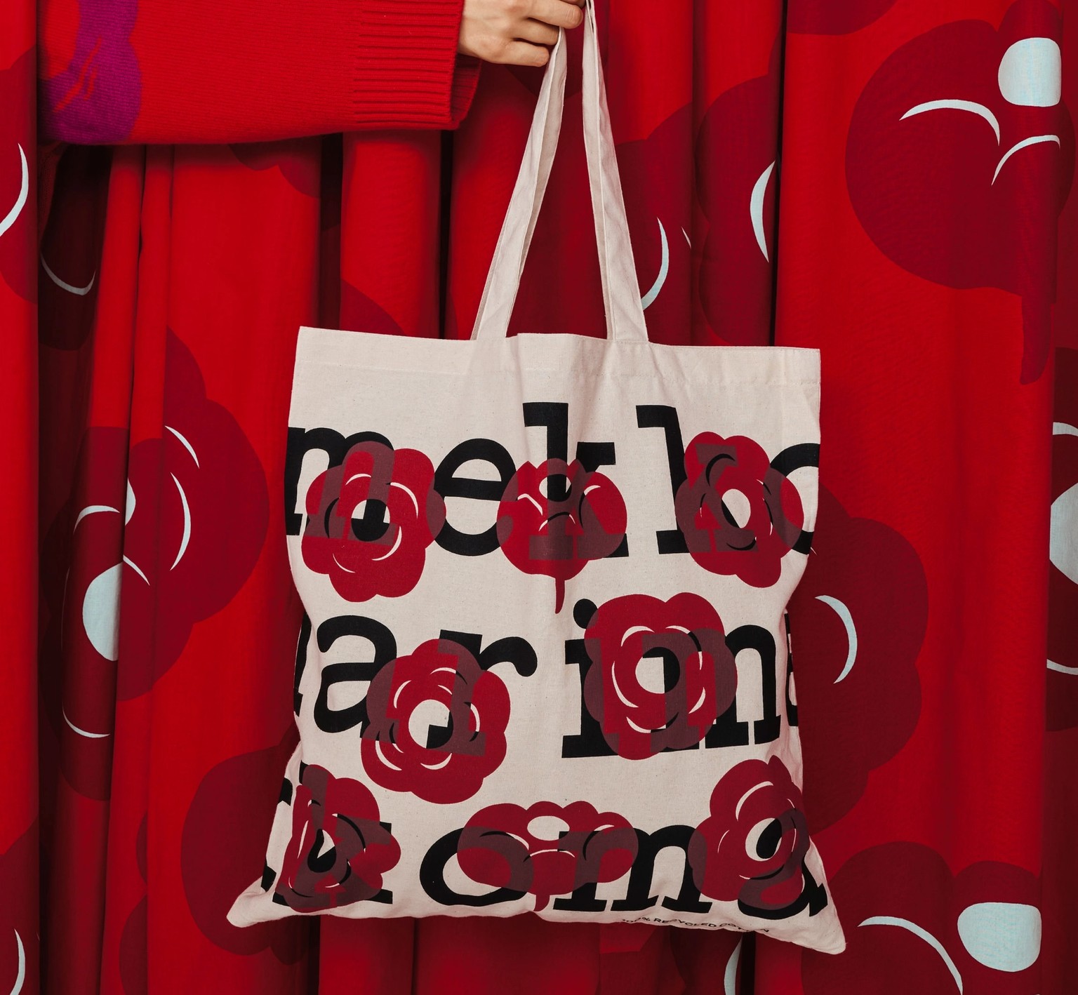 A hand holding a Marimekko logo tote with printed red flowers.