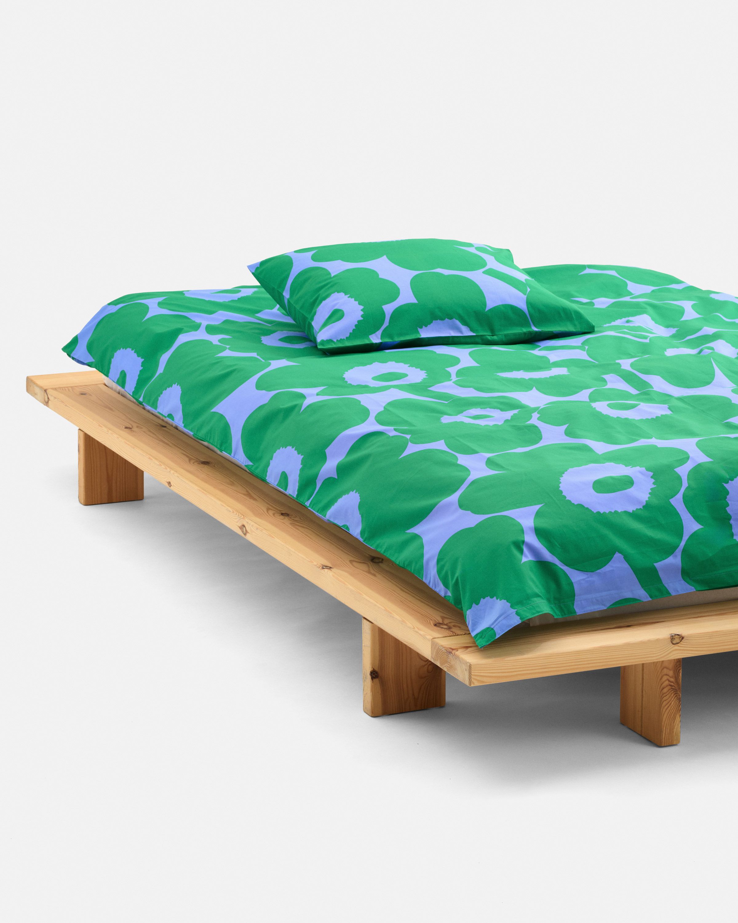 A made bed with Unikko pattern sheets green and blue.