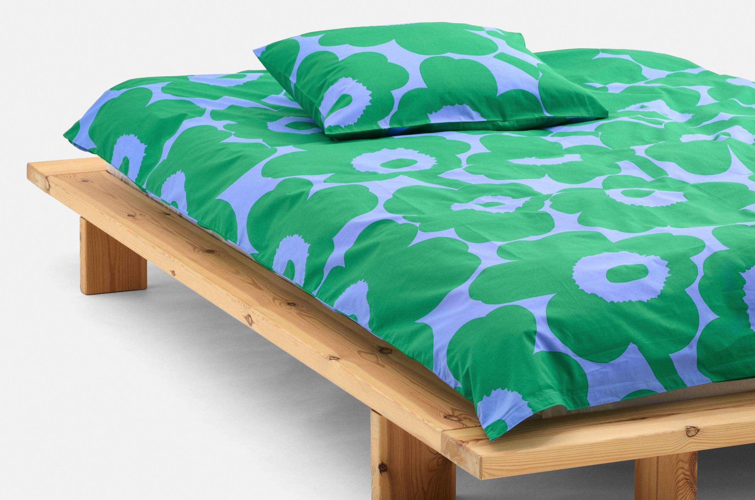 A made bed with Unikko pattern sheets green and blue.