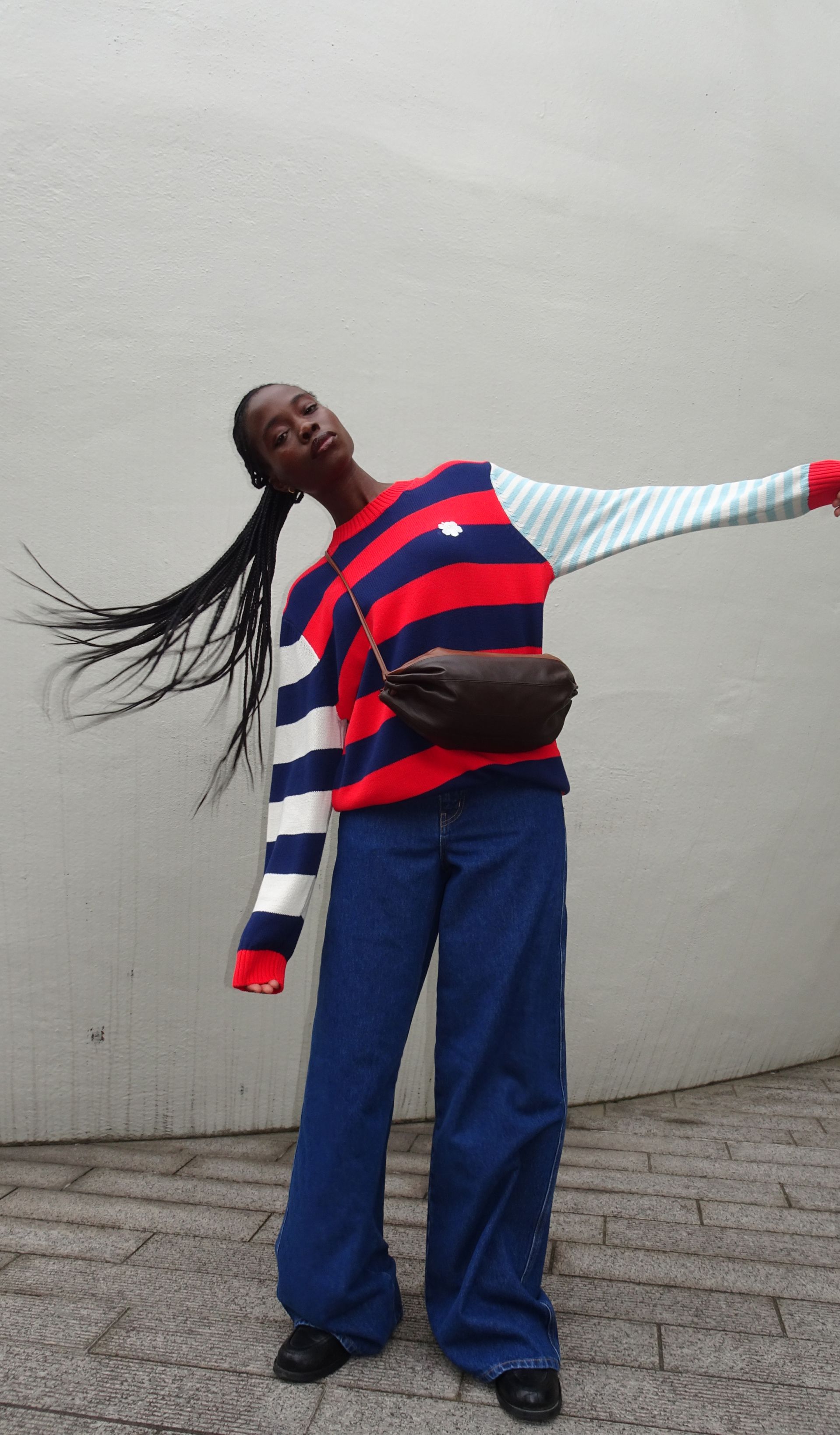 Cynthia Taylu tosses her hair, wearing blue Maridenim jeans and a colorful sweater