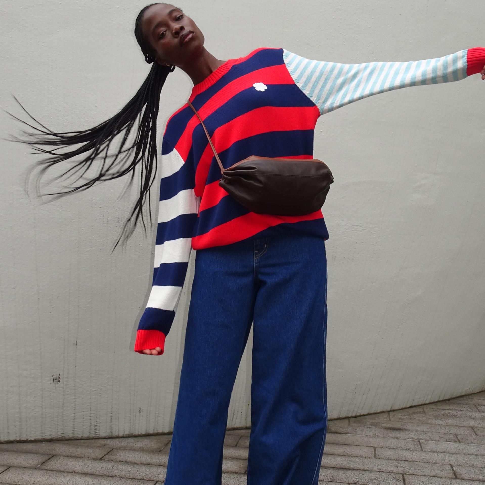 Cynthia Taylu tosses her hair, wearing blue Maridenim jeans and a colorful sweater