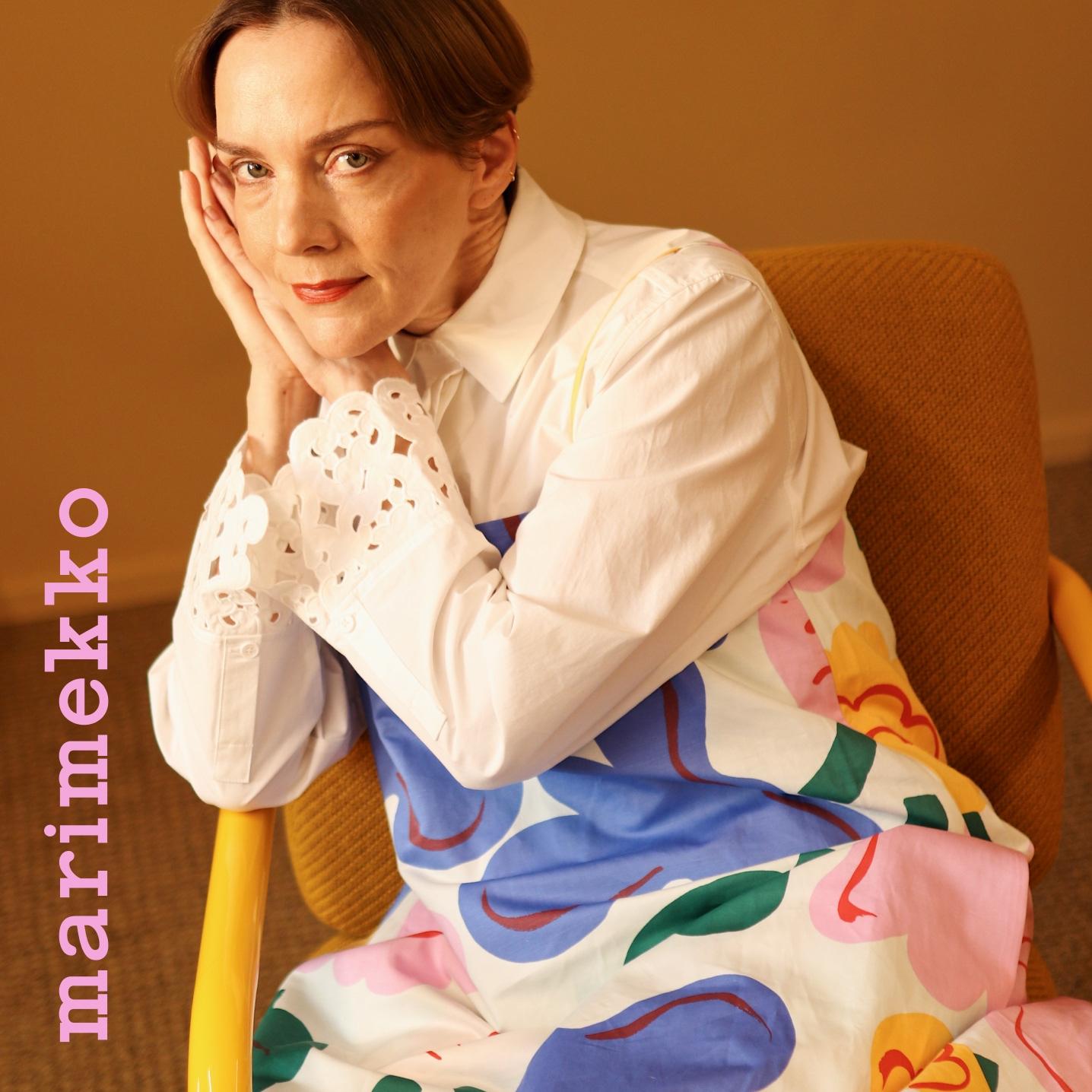 A woman (Maria Veitola) wearing a dress in Kukasta kukkaan print, a shirt with Keidas embroidery and on the image the text ''Marimekko'' vertically in the left bottom corner.