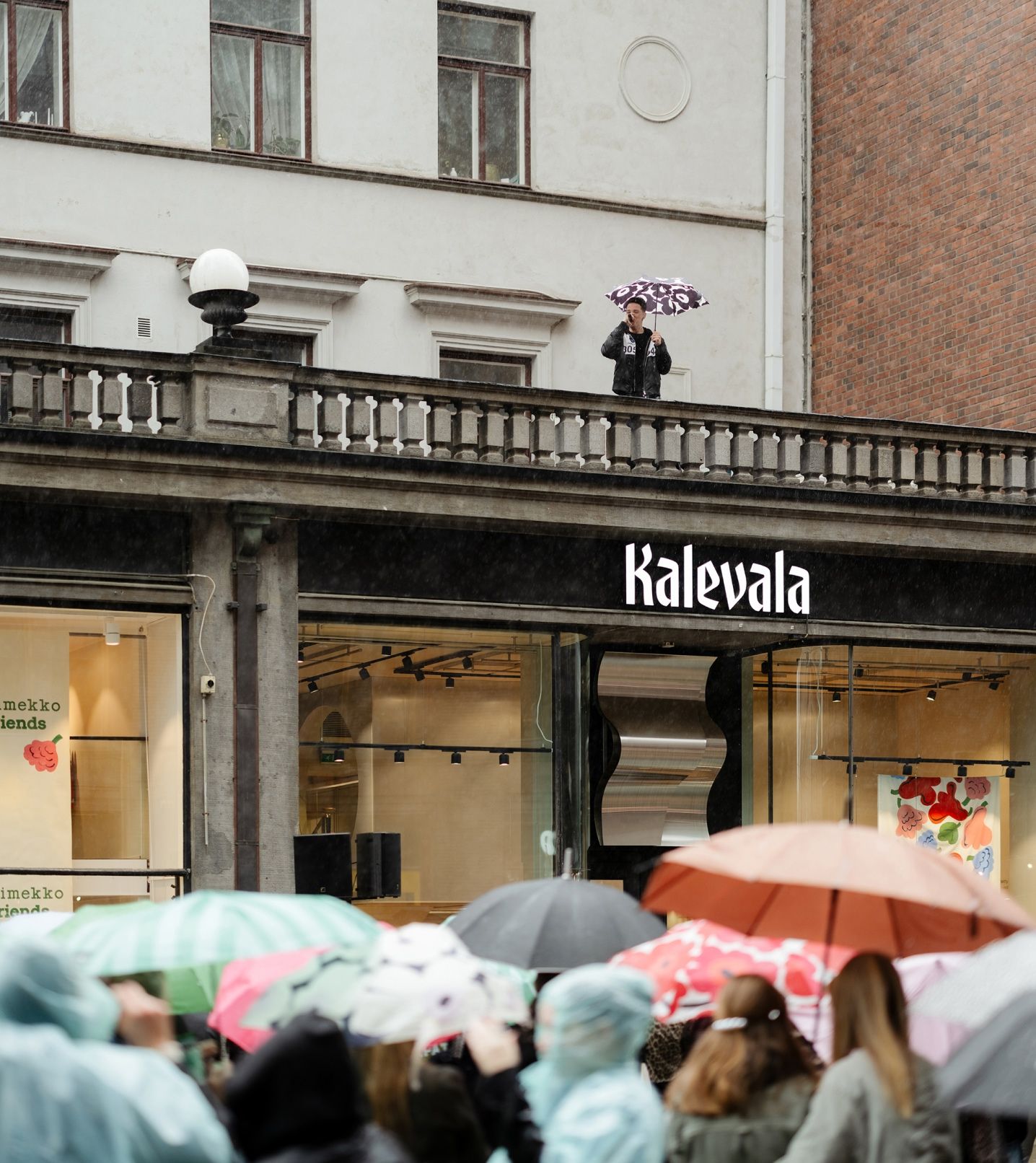 Ares esiintymässä Marimekko & friends -tapahtumassa Aleksinkulman myymälän katolla ja ihmisiä katsomassa sateenvarjojen kanssa.