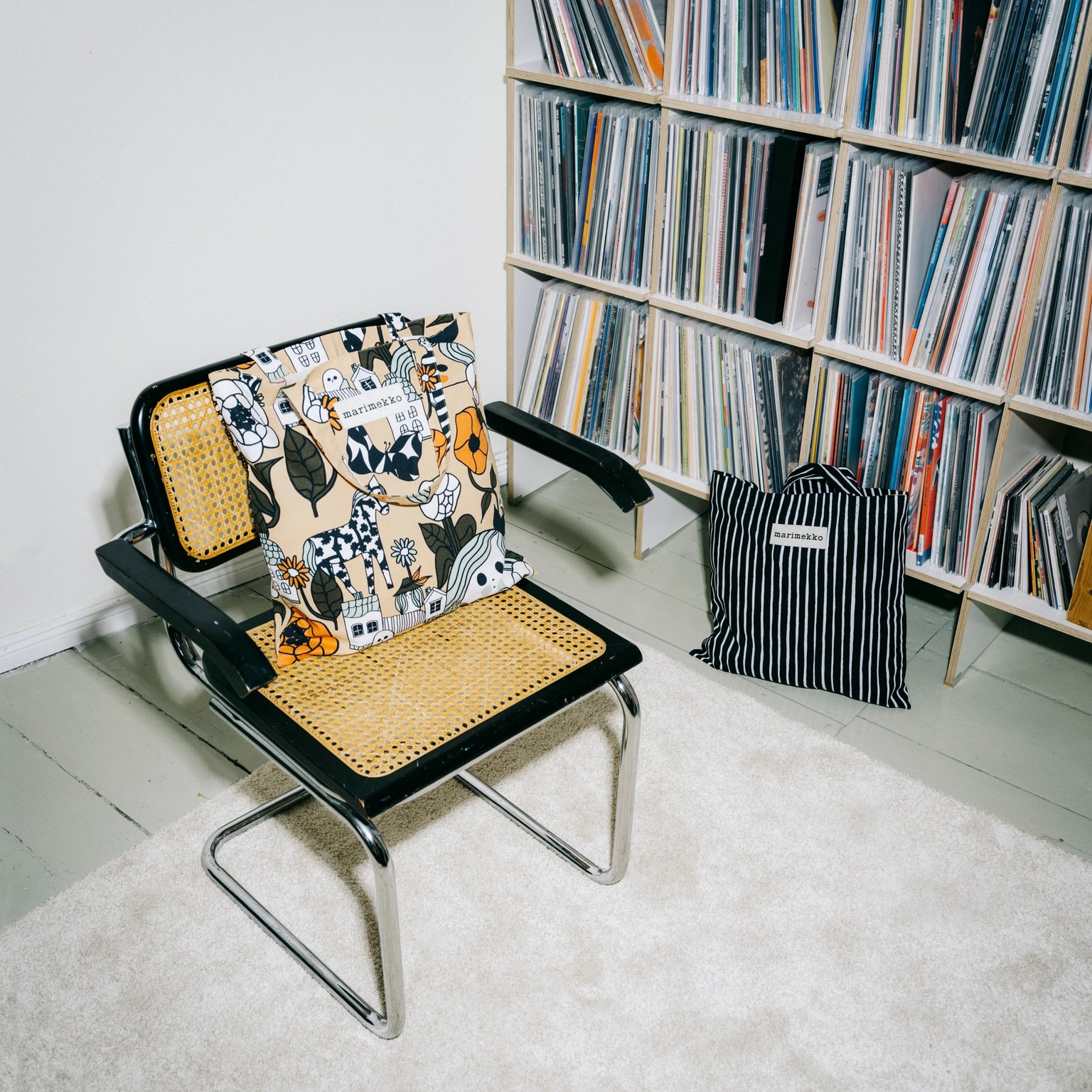 Marimade canvas bags placed on a chair and on the floor in front of a bookshelf.