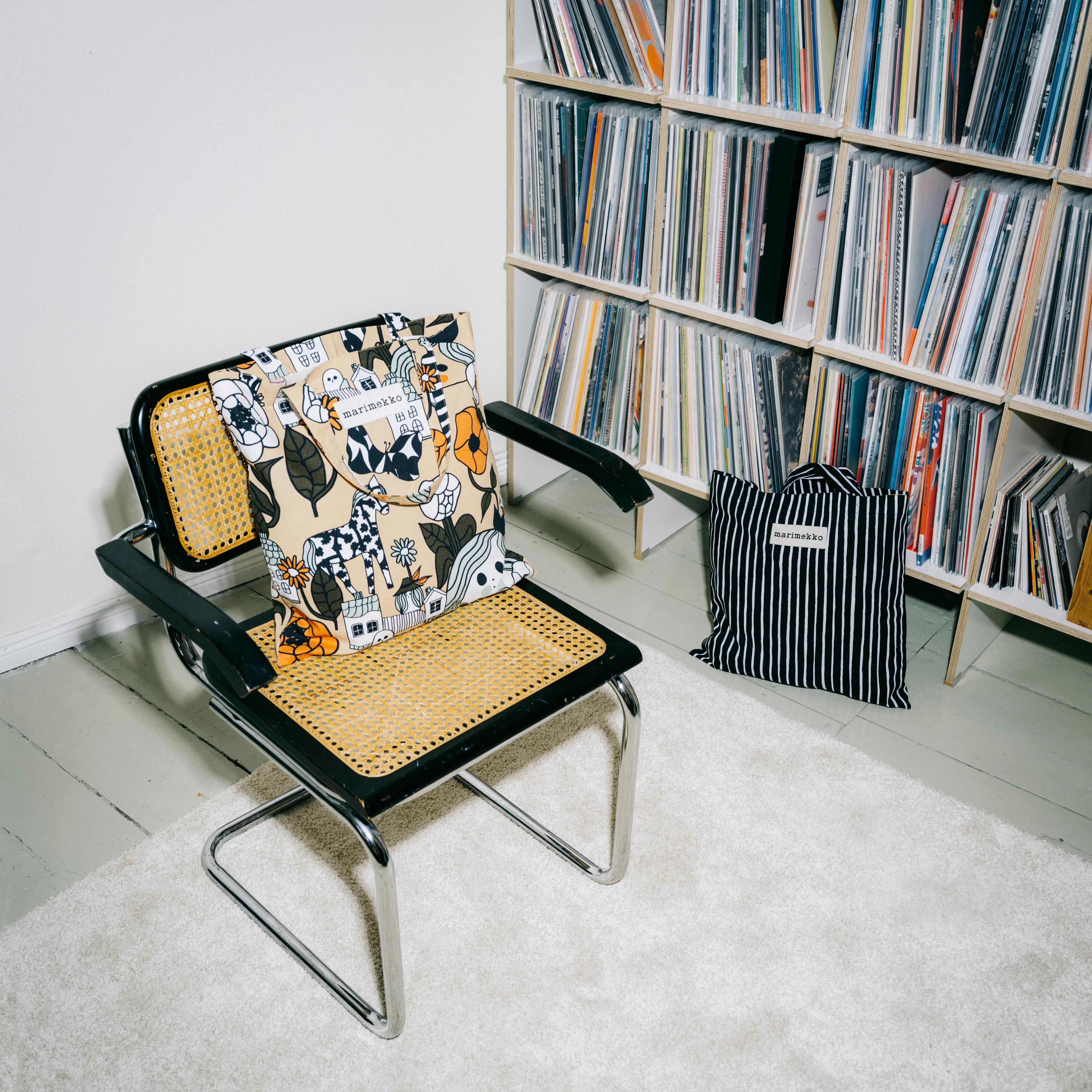 Marimade-kangaskassi tuolilla ja lattialla kirjahyllyn edessä.