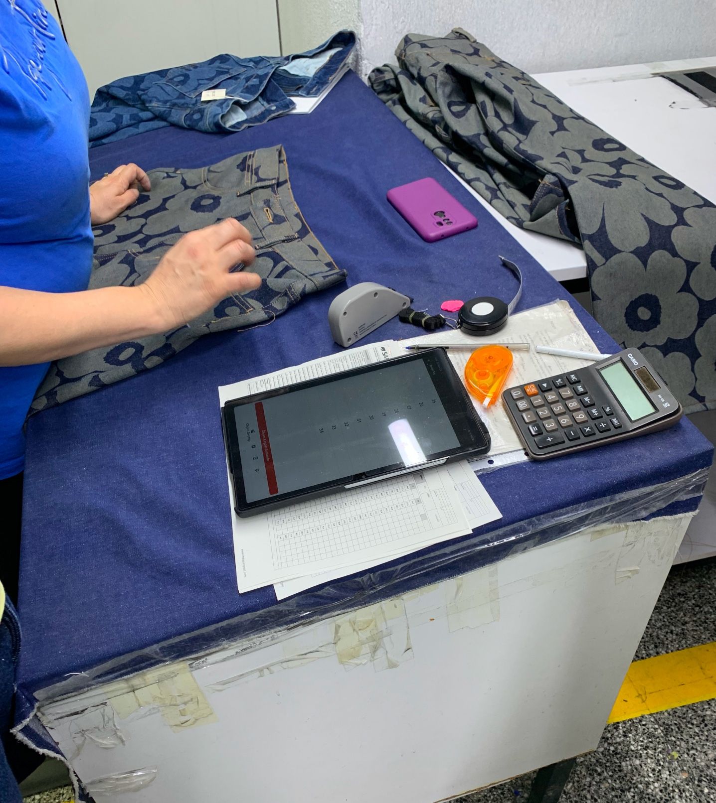 A siluette of a woman by a table with jean fabric pieces, stationary items and a pair of Maridenim jeans.