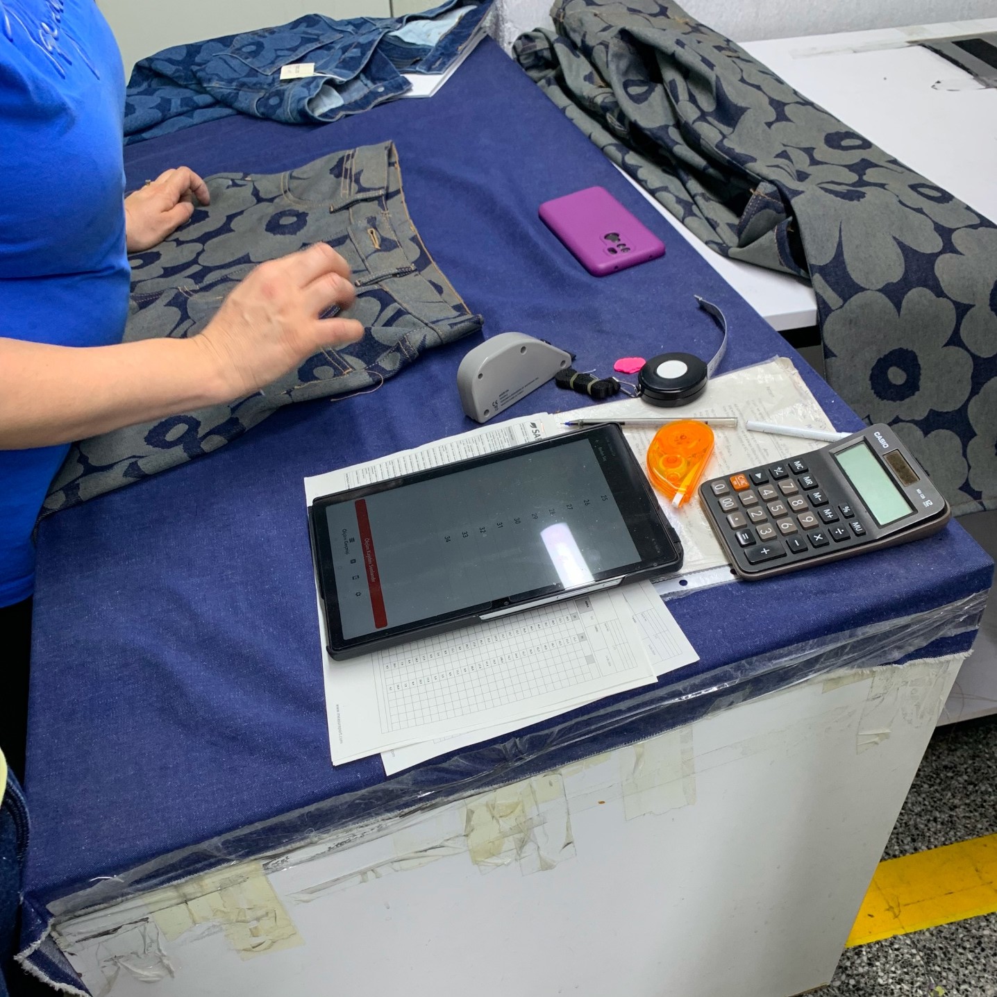 A siluette of a woman by a table with jean fabric pieces, stationary items and a pair of Maridenim jeans.