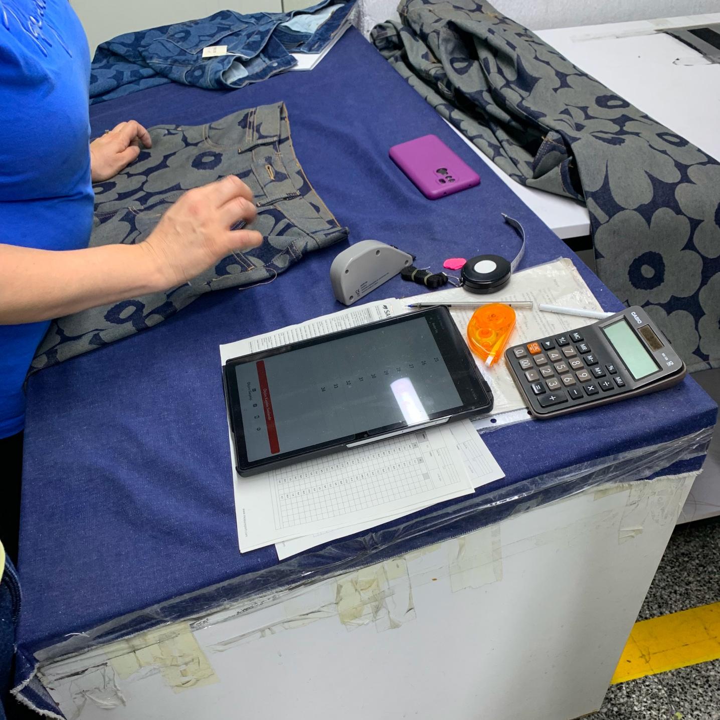 Une silhouette de femme près d’une table avec des morceaux de tissu en jean, des articles de papeterie et un jean Maridenim.