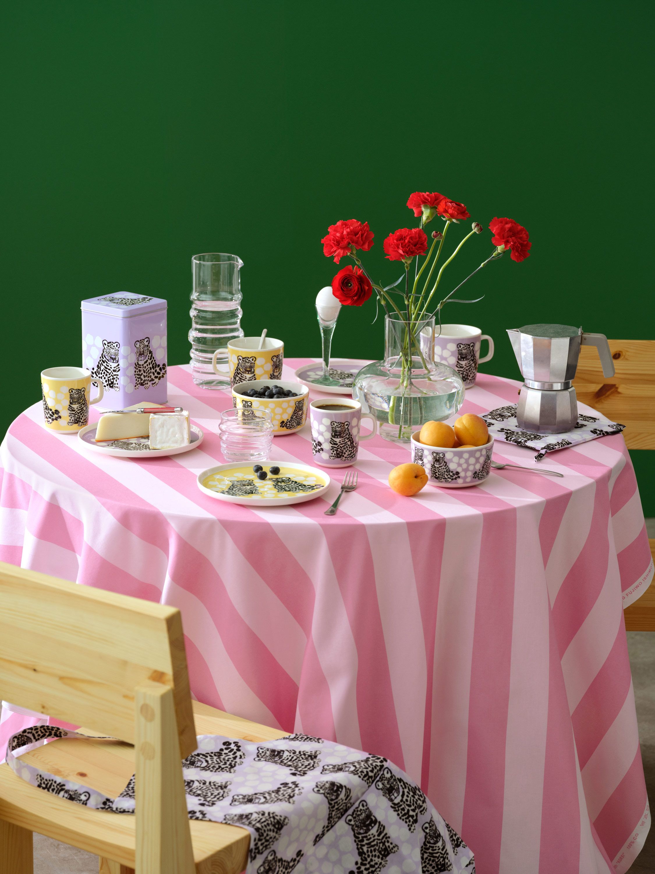 Katettu pöytä, jossa on vaaleanpunainen Korsi-pöytäliina ja keltaisia ja violetteja Kaksoset-astioita.