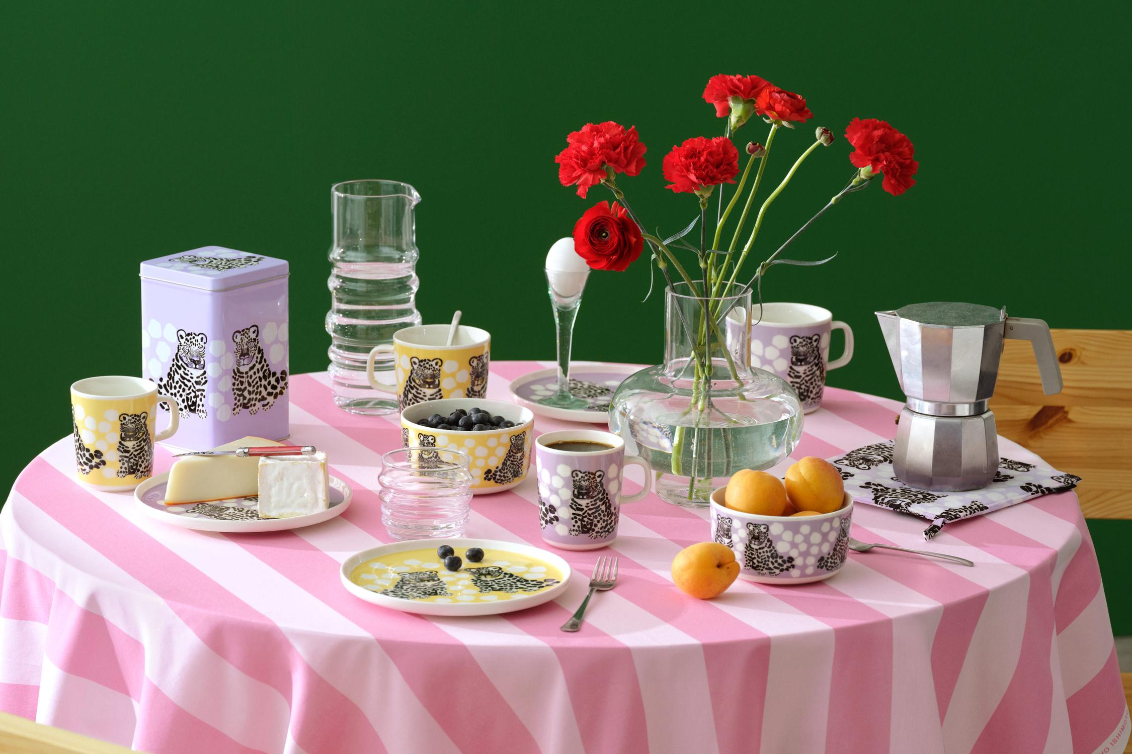 Katettu pöytä, jossa on vaaleanpunainen Korsi-pöytäliina ja keltaisia ja violetteja Kaksoset-astioita.