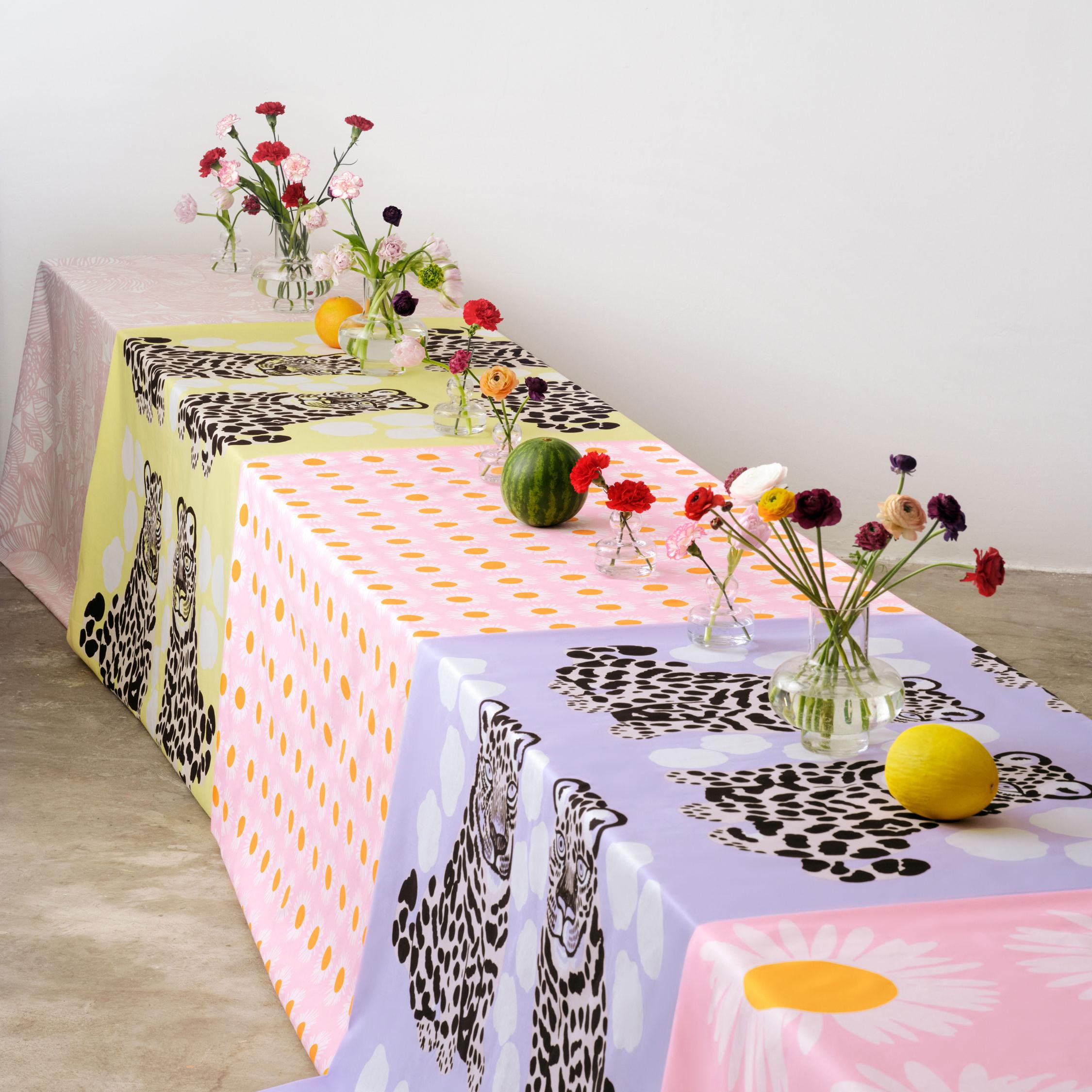 Pitkä pöytä, jossa useita kukkamaljakkoja ja Kaksoset sekä Auringonkukka kankaita pöytäliinoina.