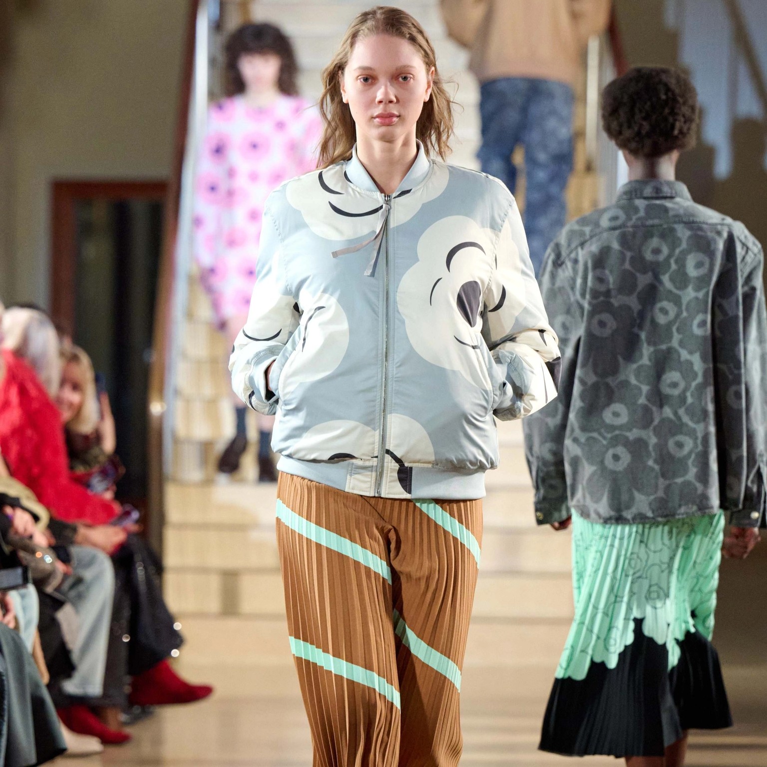 A model walking in Marimekko's fashion show wearing grey and white coat and brown Myy-skirt