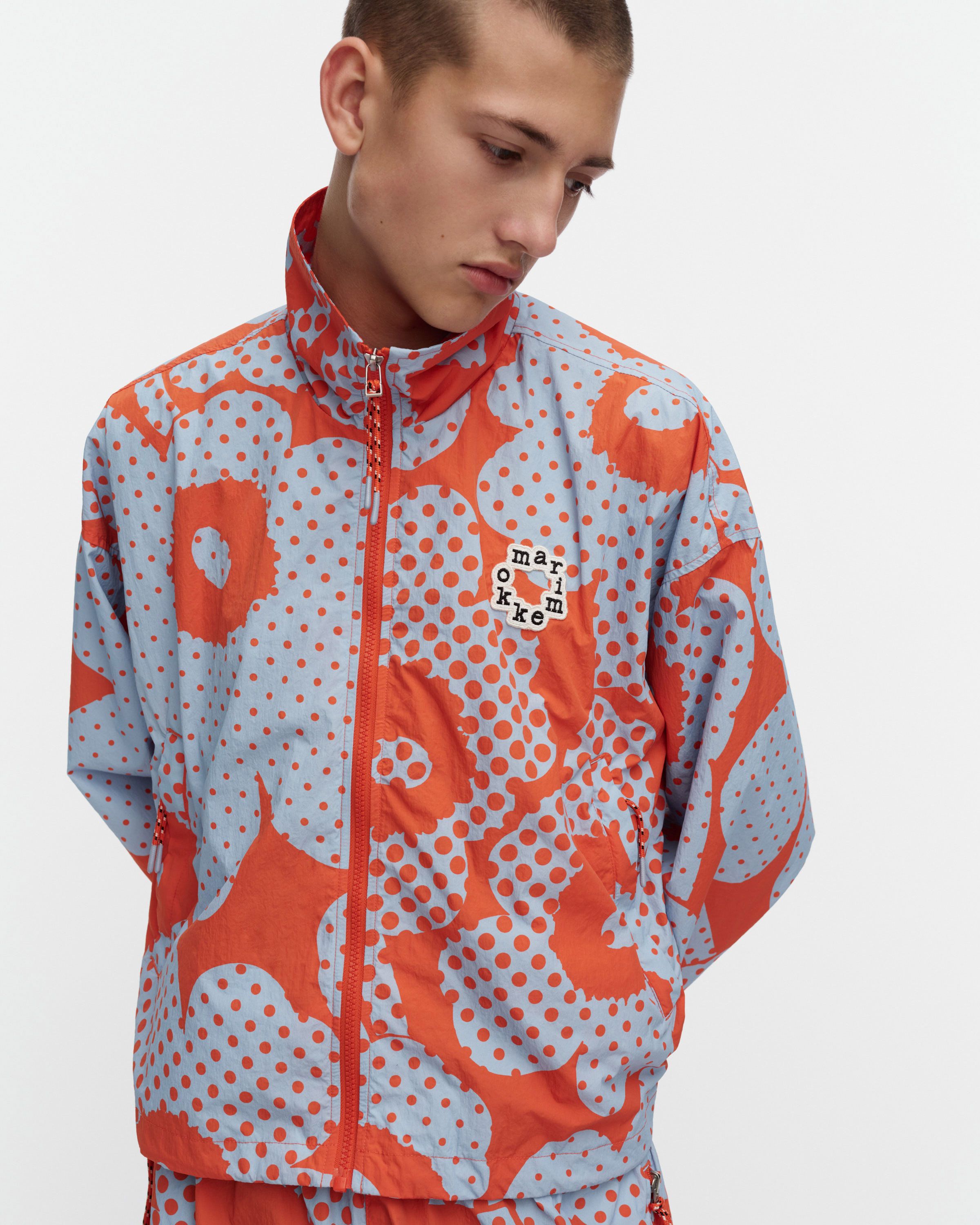 Model wearing Marimekko Kioski Active coat in red and blue Unikko print.