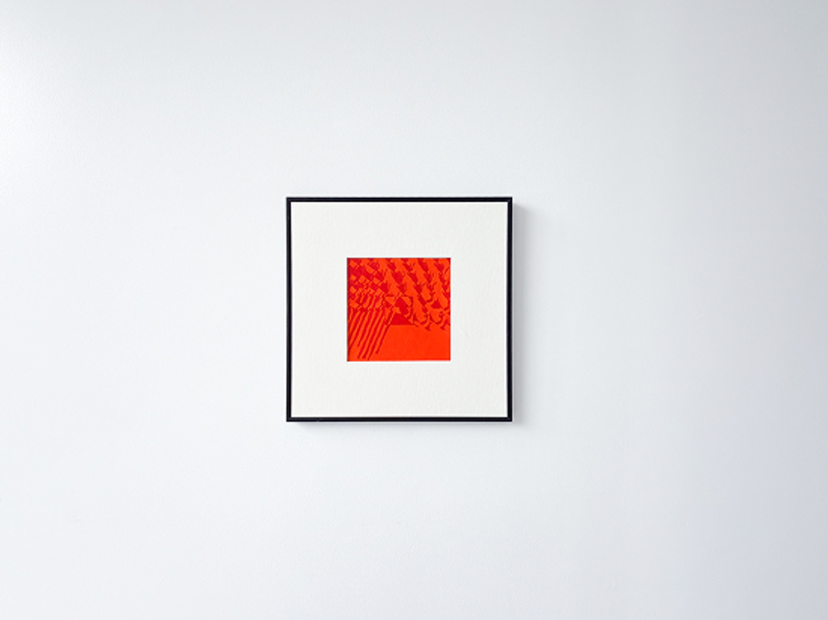Black-framed abstract art with red and orange geometric patterns on a white wall.