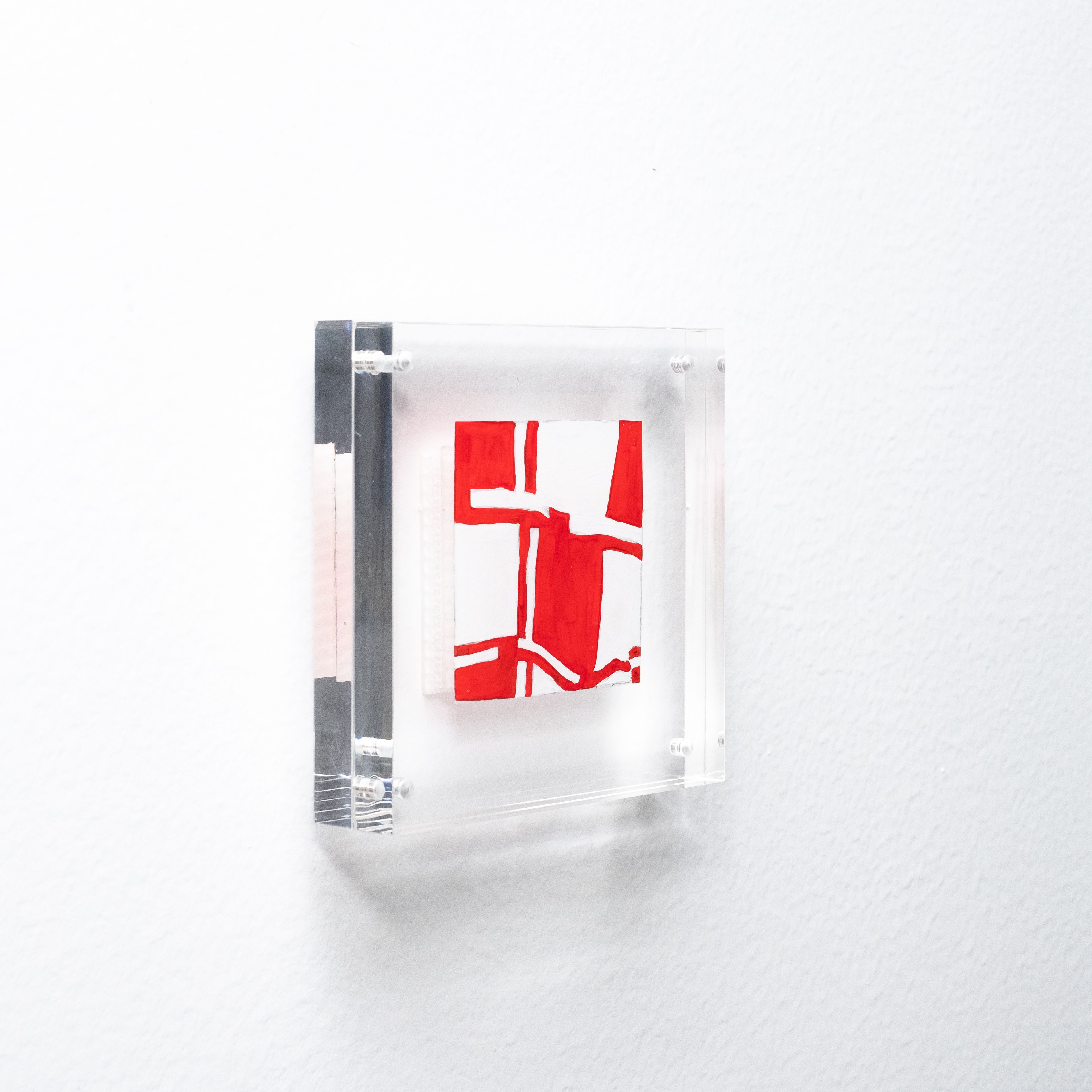 Abstract red and white artwork in a clear acrylic frame on a white wall.