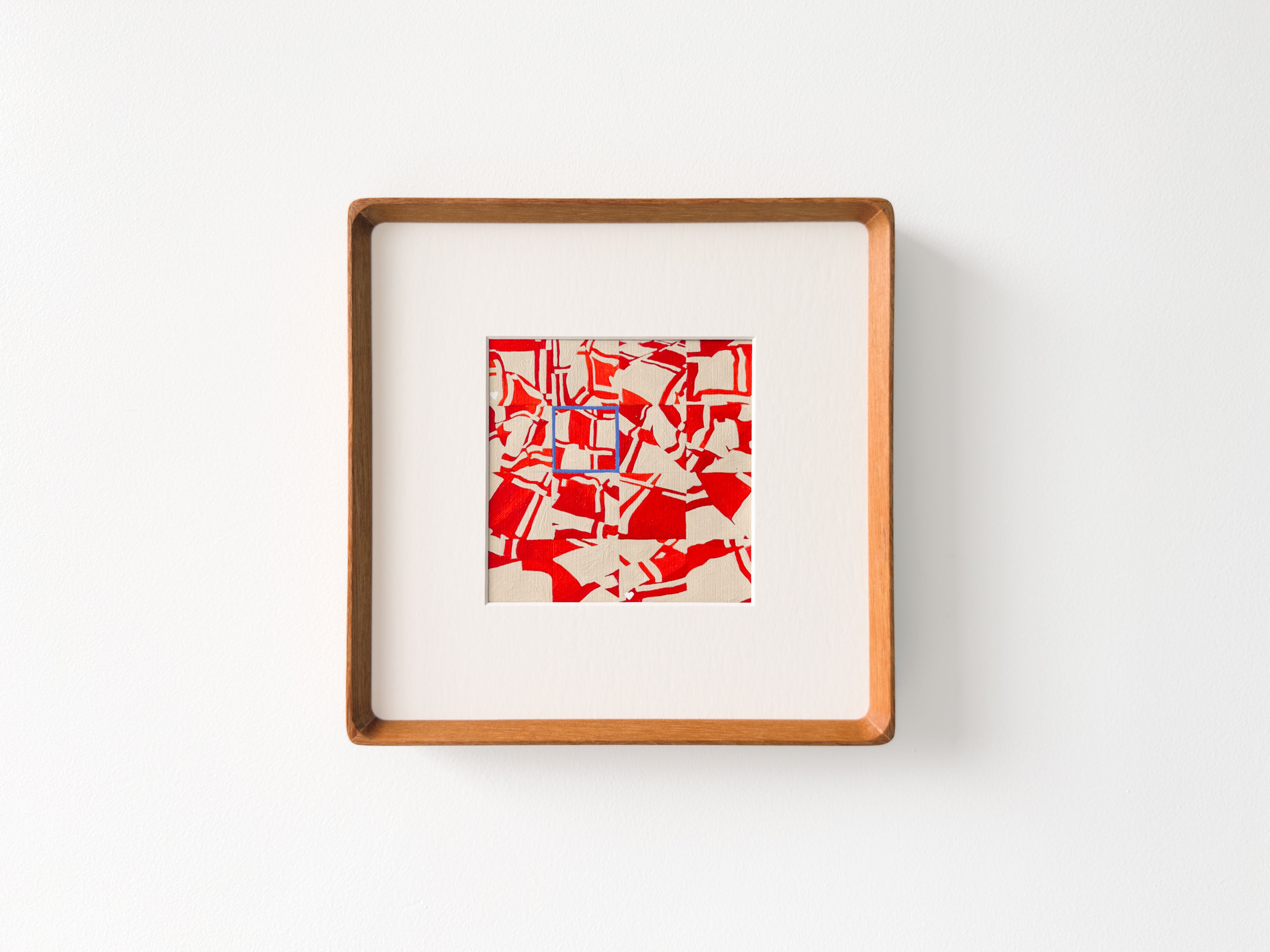 Artwork Title: Select. A small abstract artwork is centered within a wide white mat and a square wooden frame on a white wall. The piece features a dense red and cream pattern of fragmented, angular shapes, with a small blue-outlined square near the center.