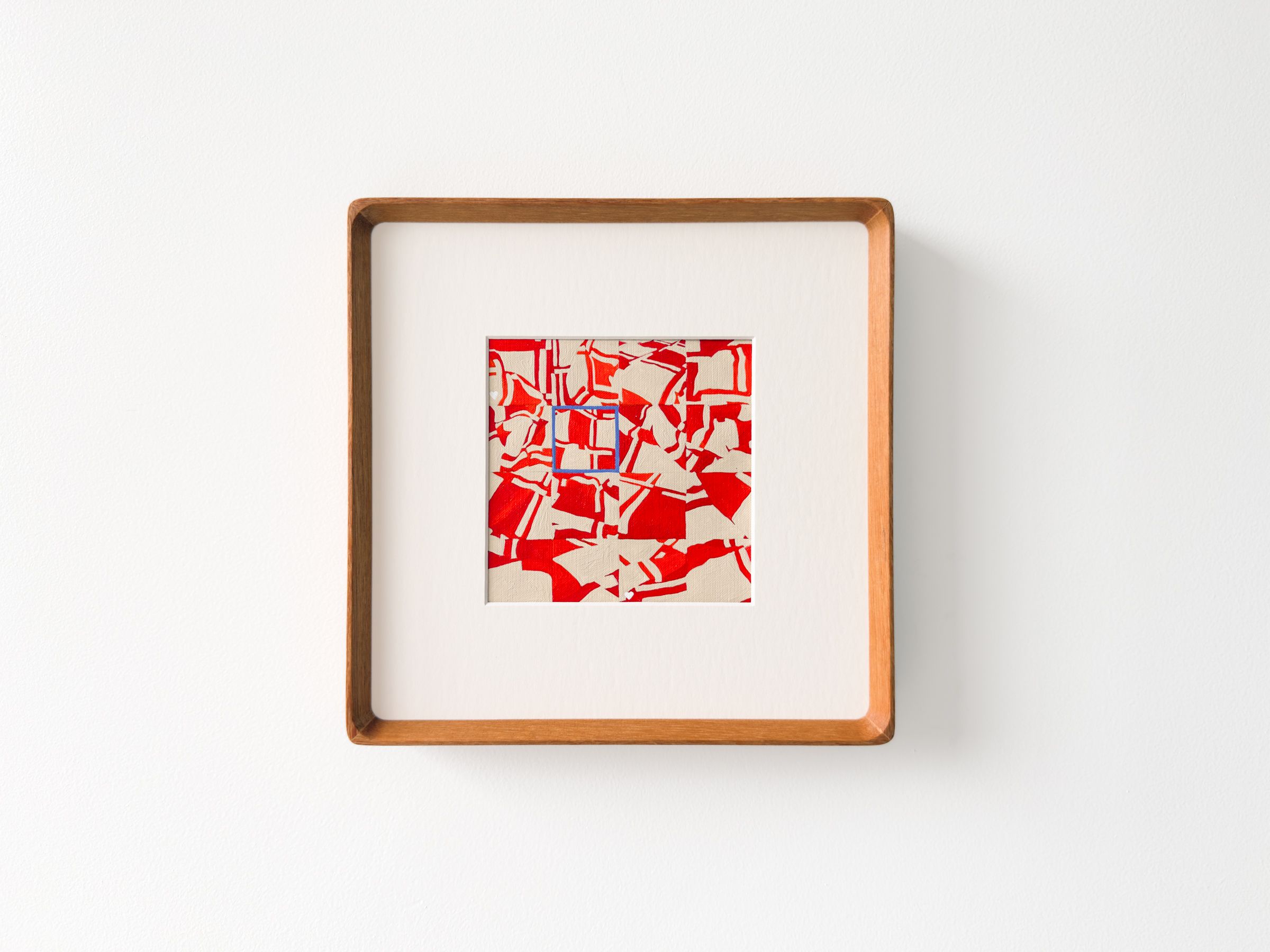 Artwork Title: Select. A small abstract artwork is centered within a wide white mat and a square wooden frame on a white wall. The piece features a dense red and cream pattern of fragmented, angular shapes, with a small blue-outlined square near the center.