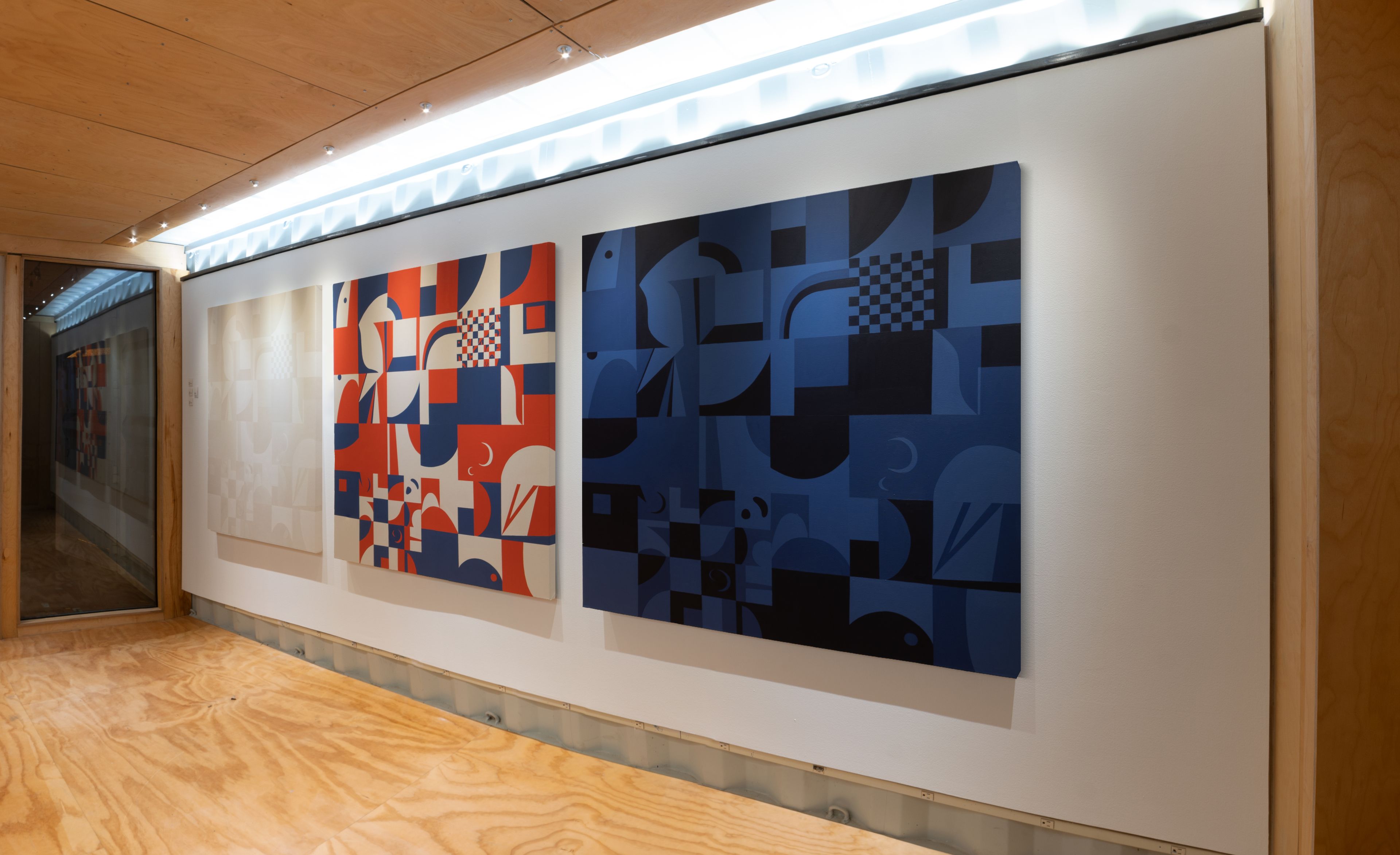 a small shipping container gallery with wood floors and white walls hold three geometric grid large paintings side by side