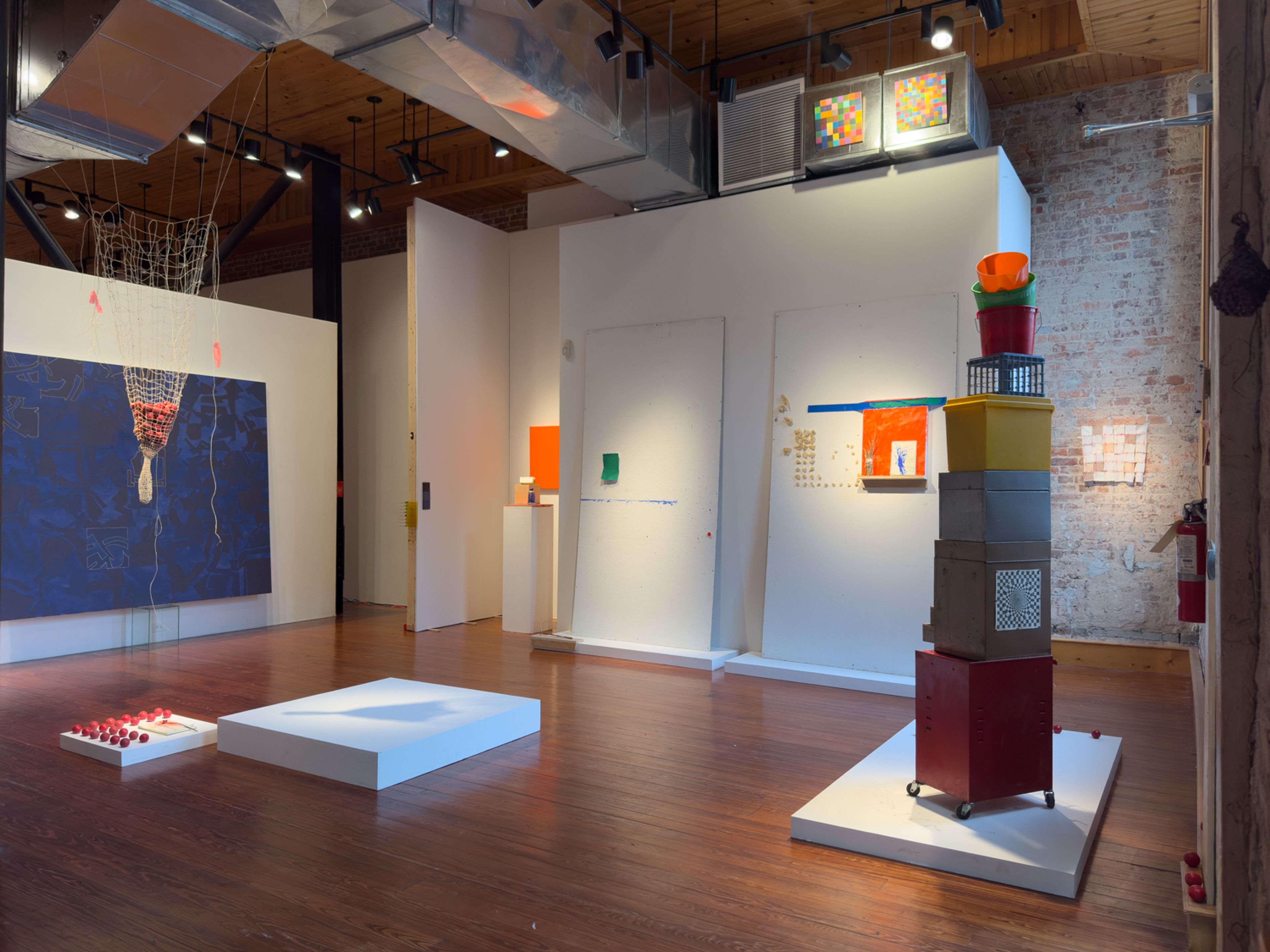 a full gallery photo including large and small paintings, hanging and stacked sculptures and works hung in non-traditional spaces such as air ducts and brick walls in storage closets