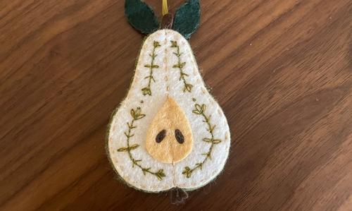 Hand embroidered ornament for a christmas tree. The ornament is a pear cut lengthwise showing the seeds.