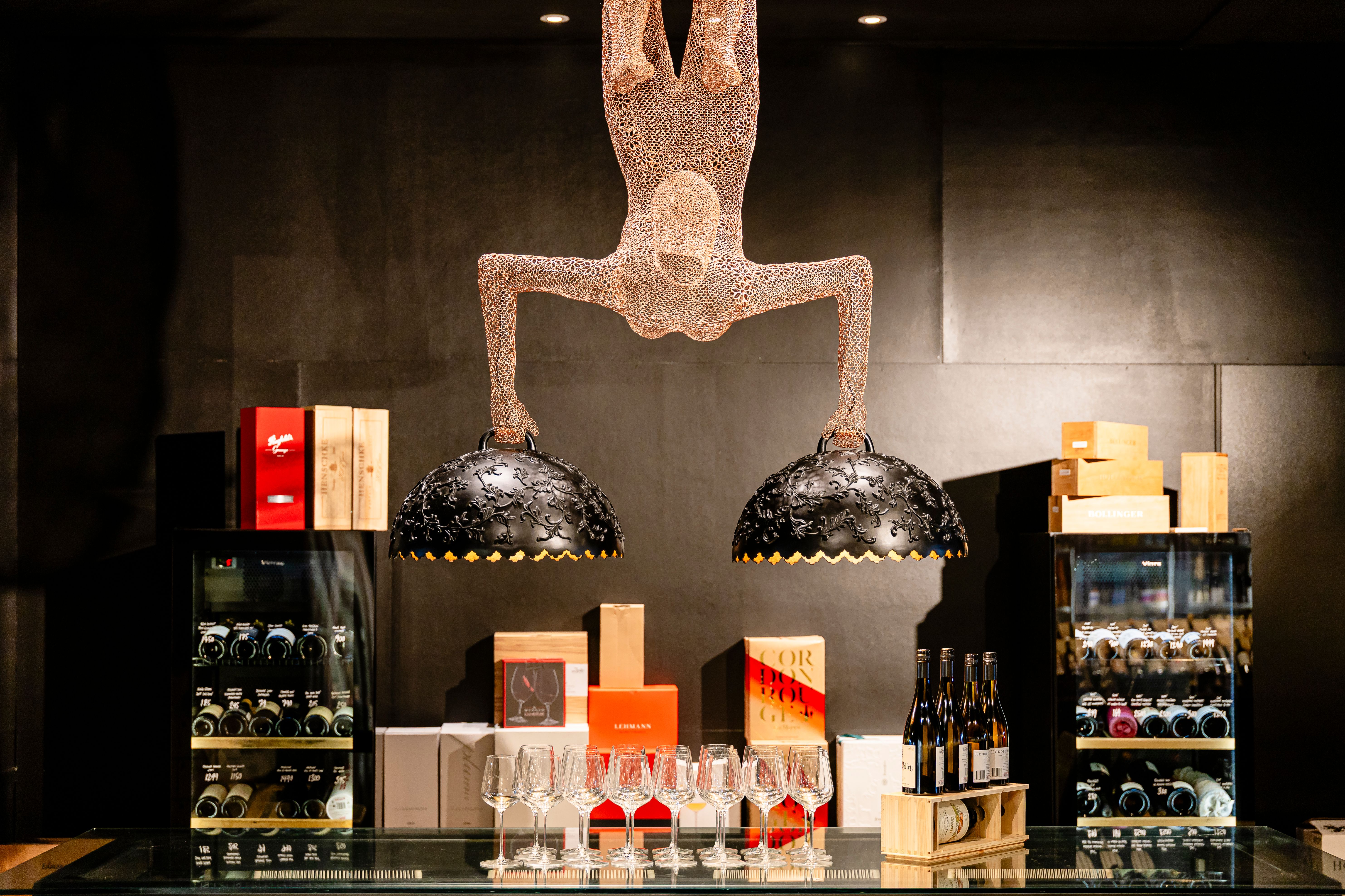 Wine tasting table with glasses and wine bottles behind, human shaped chandelier above