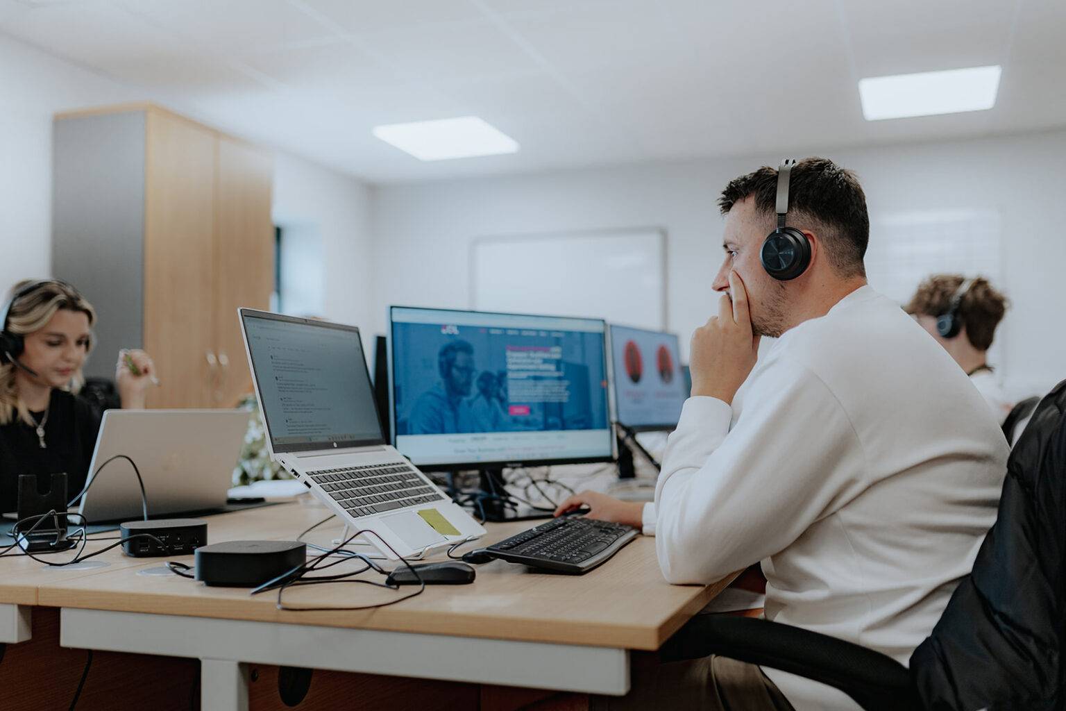 Two people working at computers with headsets in a modern office.
