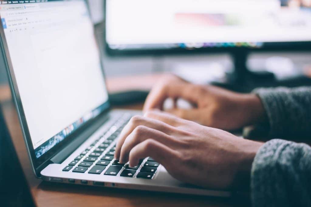 Hands typing on a keyboard with screen in the background