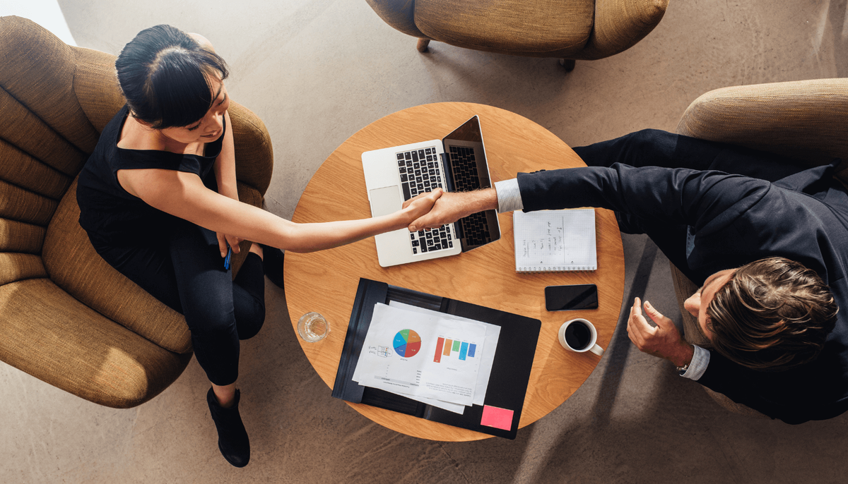 a man and a woman shake hands at a table with a laptop
