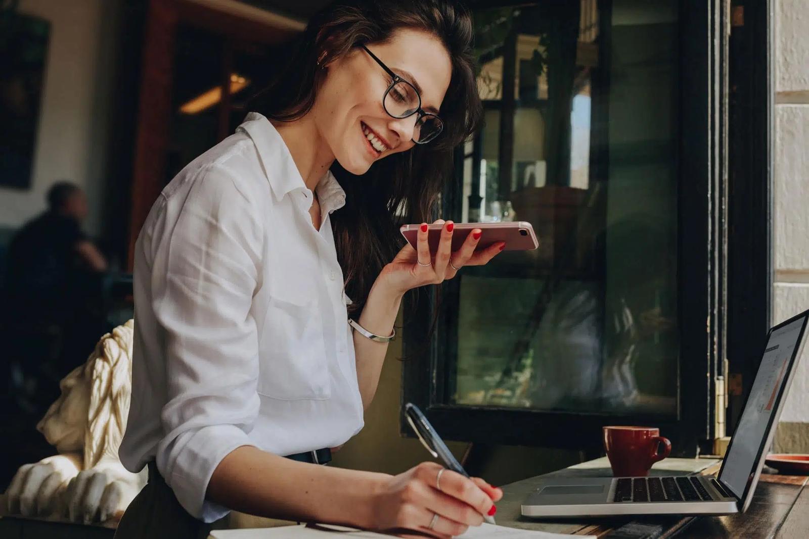 a woman is sitting at a table with a laptop and a cell phone .