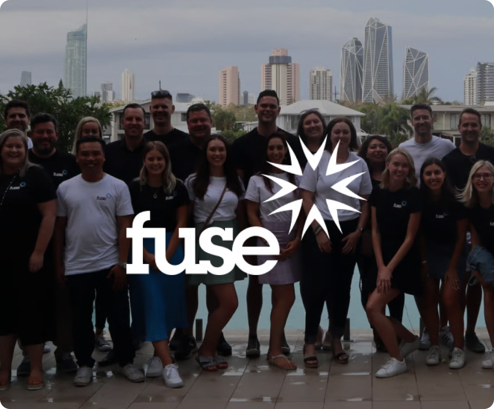 White 'fuse' logo with a starburst design overlaid on a photo of a team smiling in front of a city skyline.