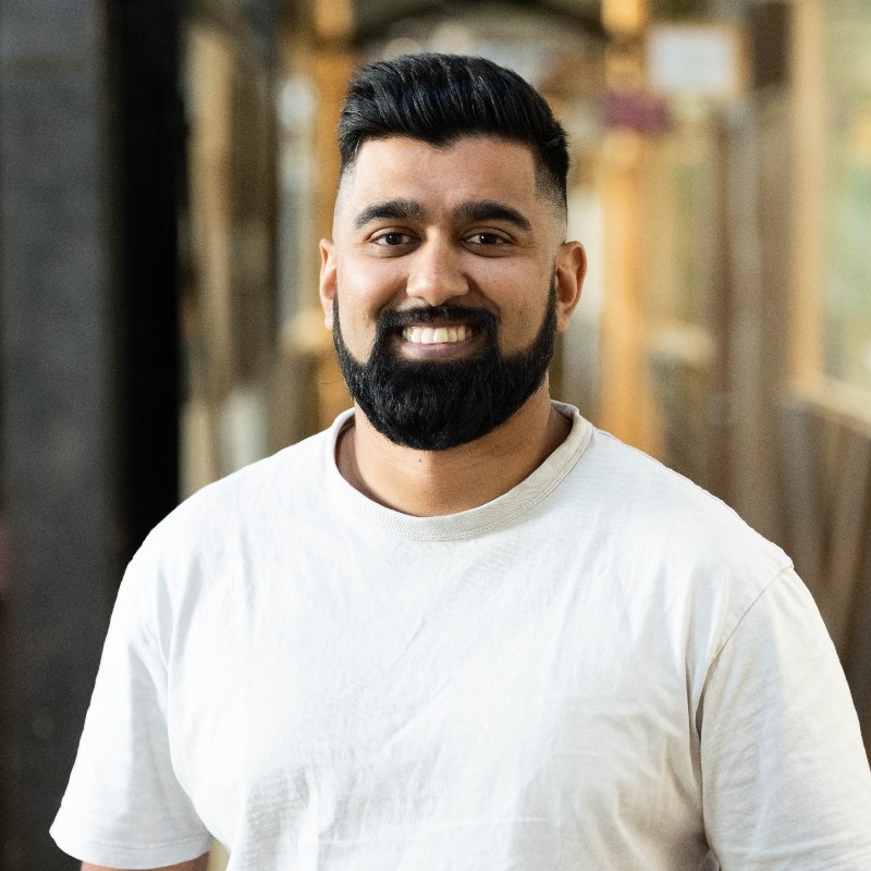 a man with a beard is wearing a white t-shirt and smiling for the camera .